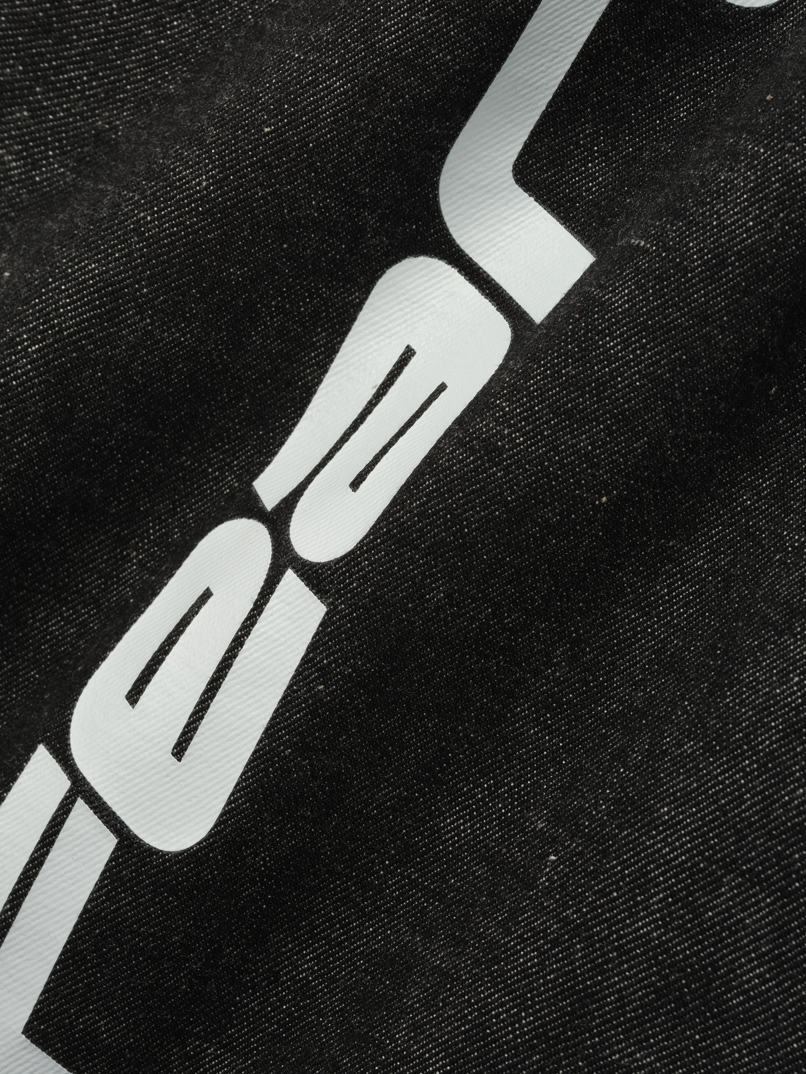 Close-up of vintage black denim work pant fabric with partial white graphic print detail on thigh area