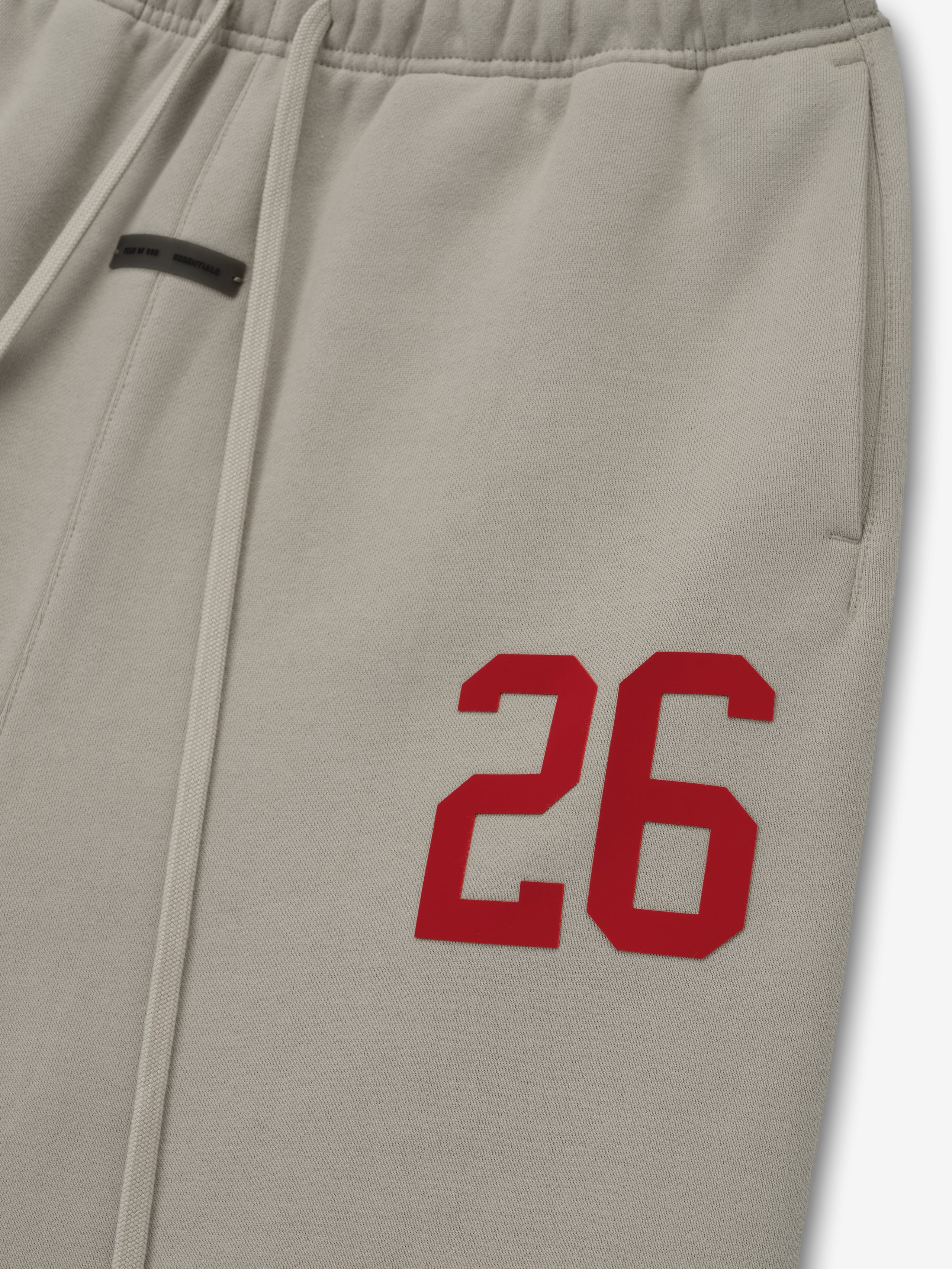 Close-up of smoke grey lounge sweatpant with elastic waistband, drawstrings, side pocket, and bold red number 26 detail