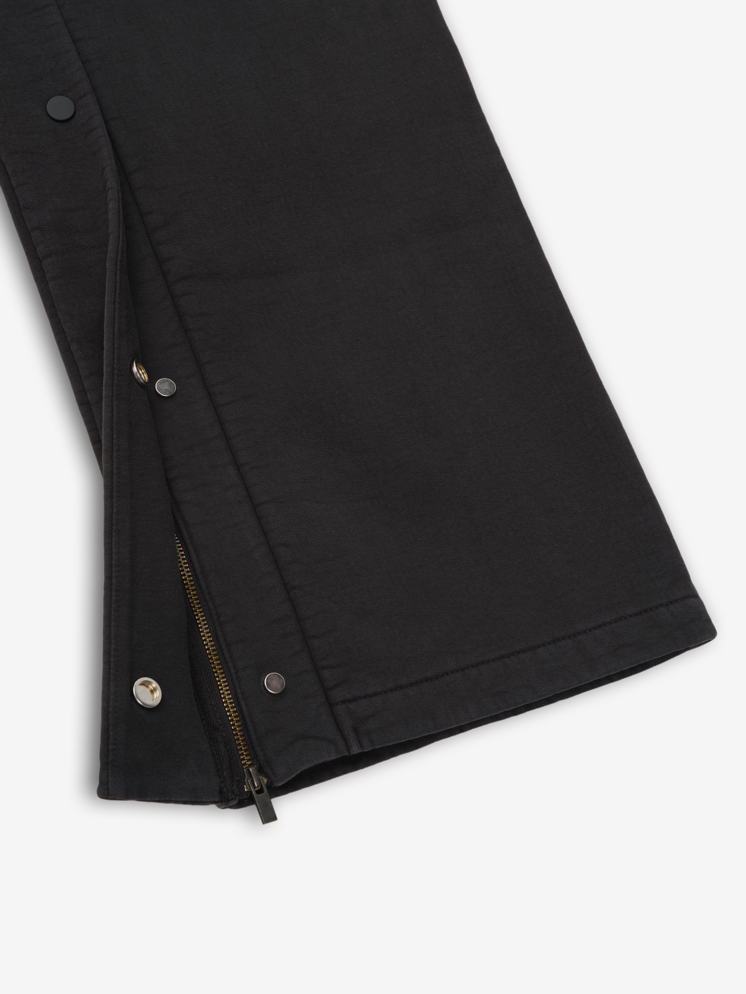 Close-up of vintage black heavy fleece tearaway sweatpant leg with partially unzipped side zipper and snap buttons