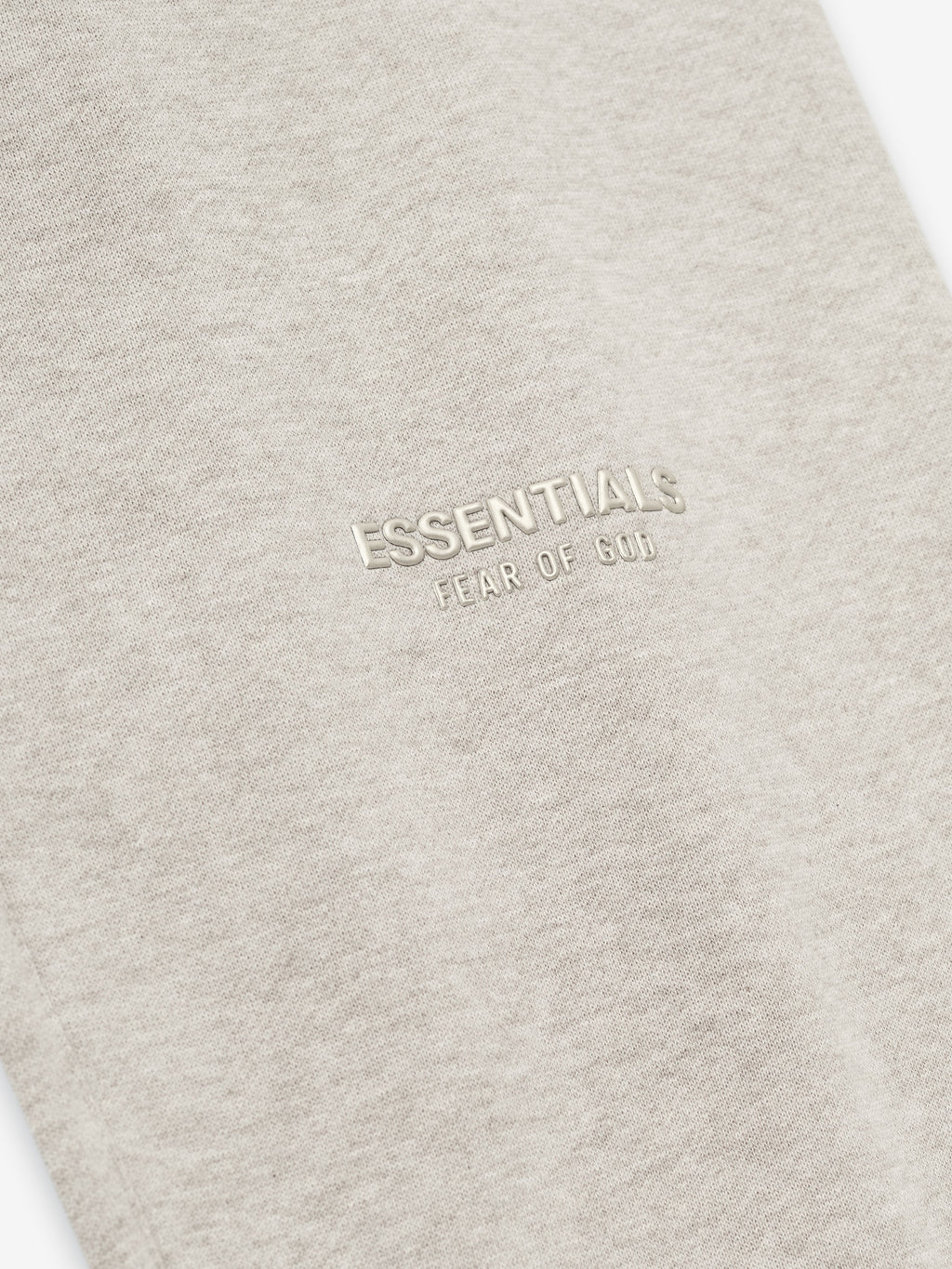 close-up of beige vintage fleece fabric with embossed ESSENTIALS Fear of God logo on the thigh area