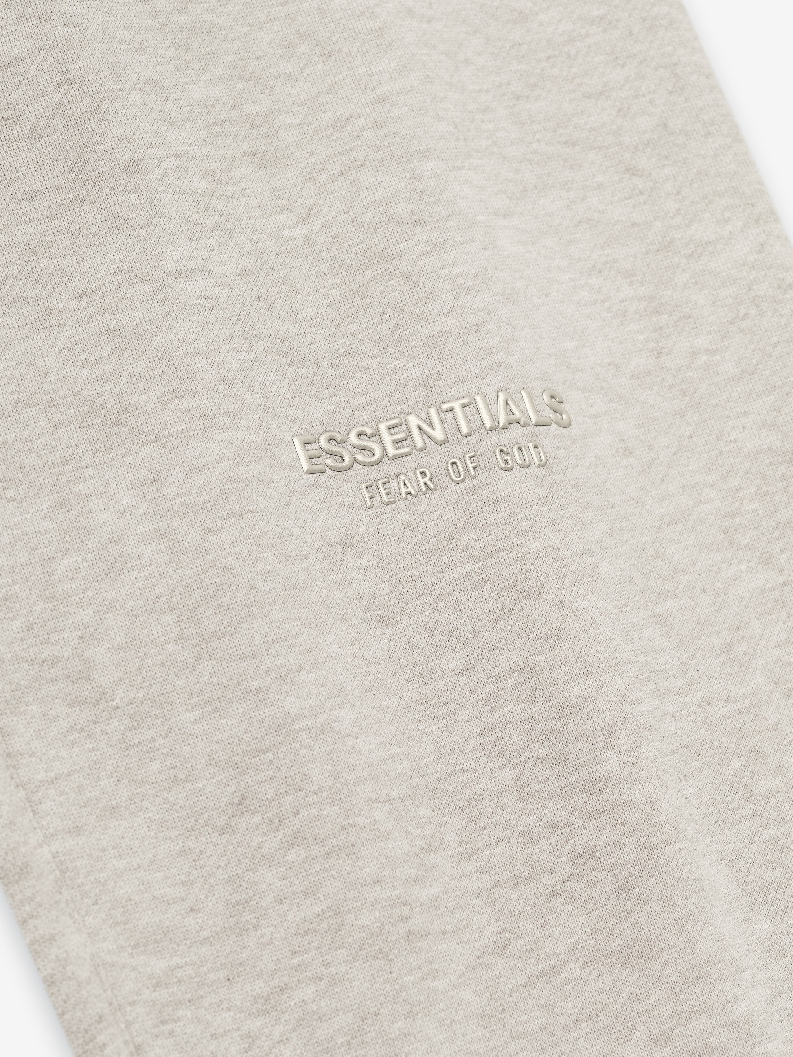 close-up of beige vintage fleece fabric with embossed ESSENTIALS Fear of God logo on the thigh area