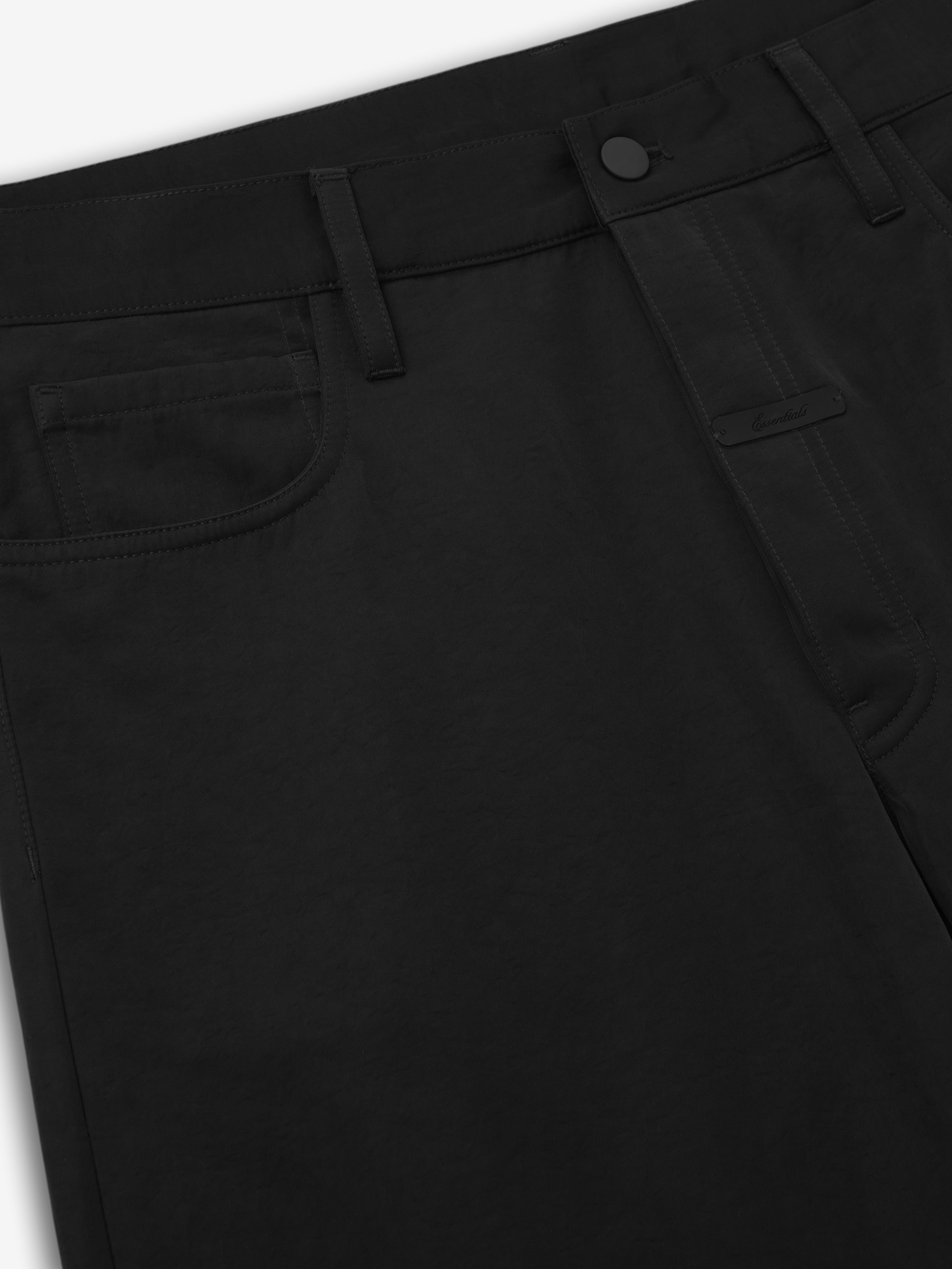 close-up of black textured nylon 5-pocket pants with straight leg and matte black button closure