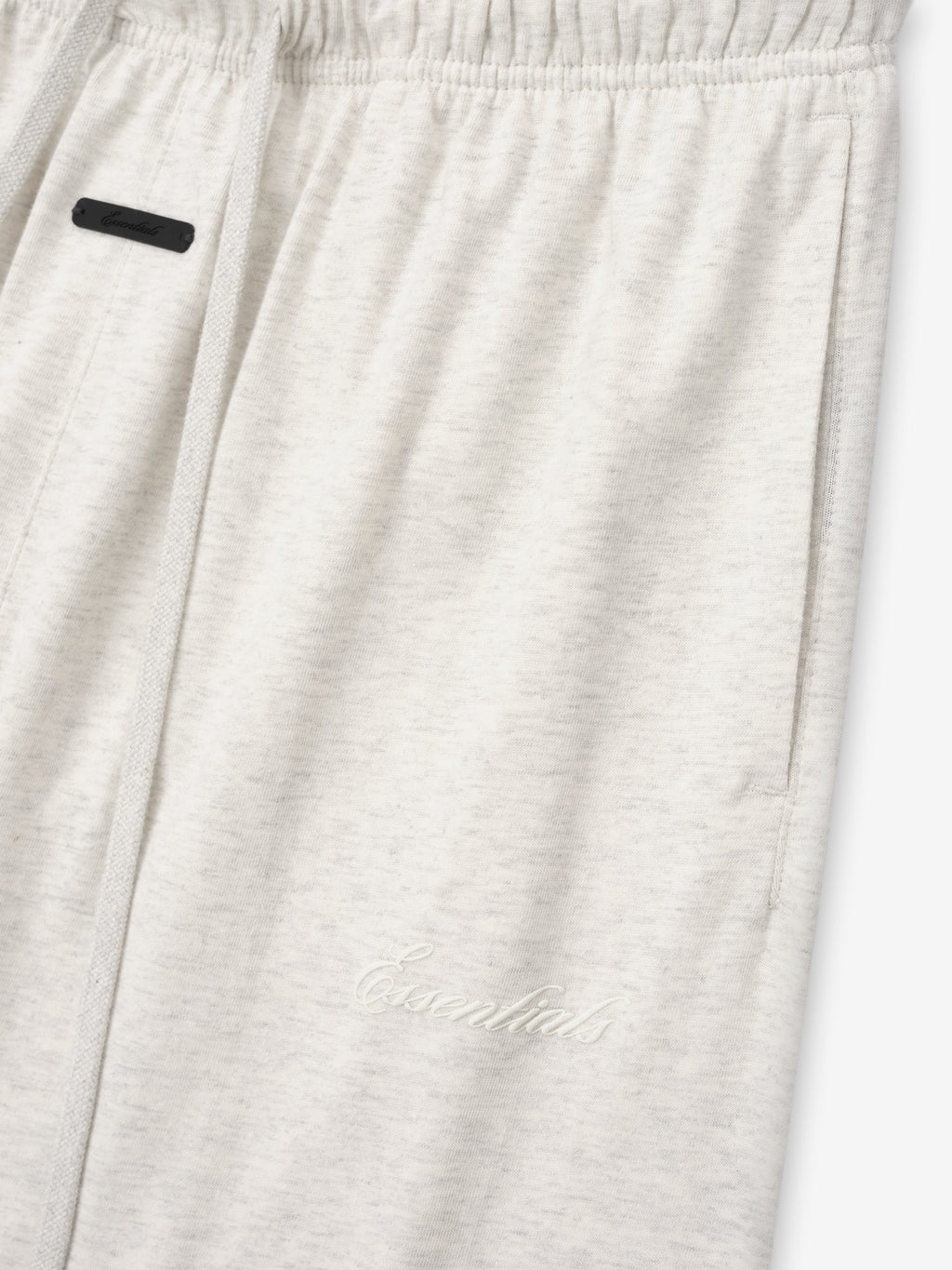 close-up of light beige women's cotton jersey sweatpants with elastic waistband and subtle embroidered Essentials logo