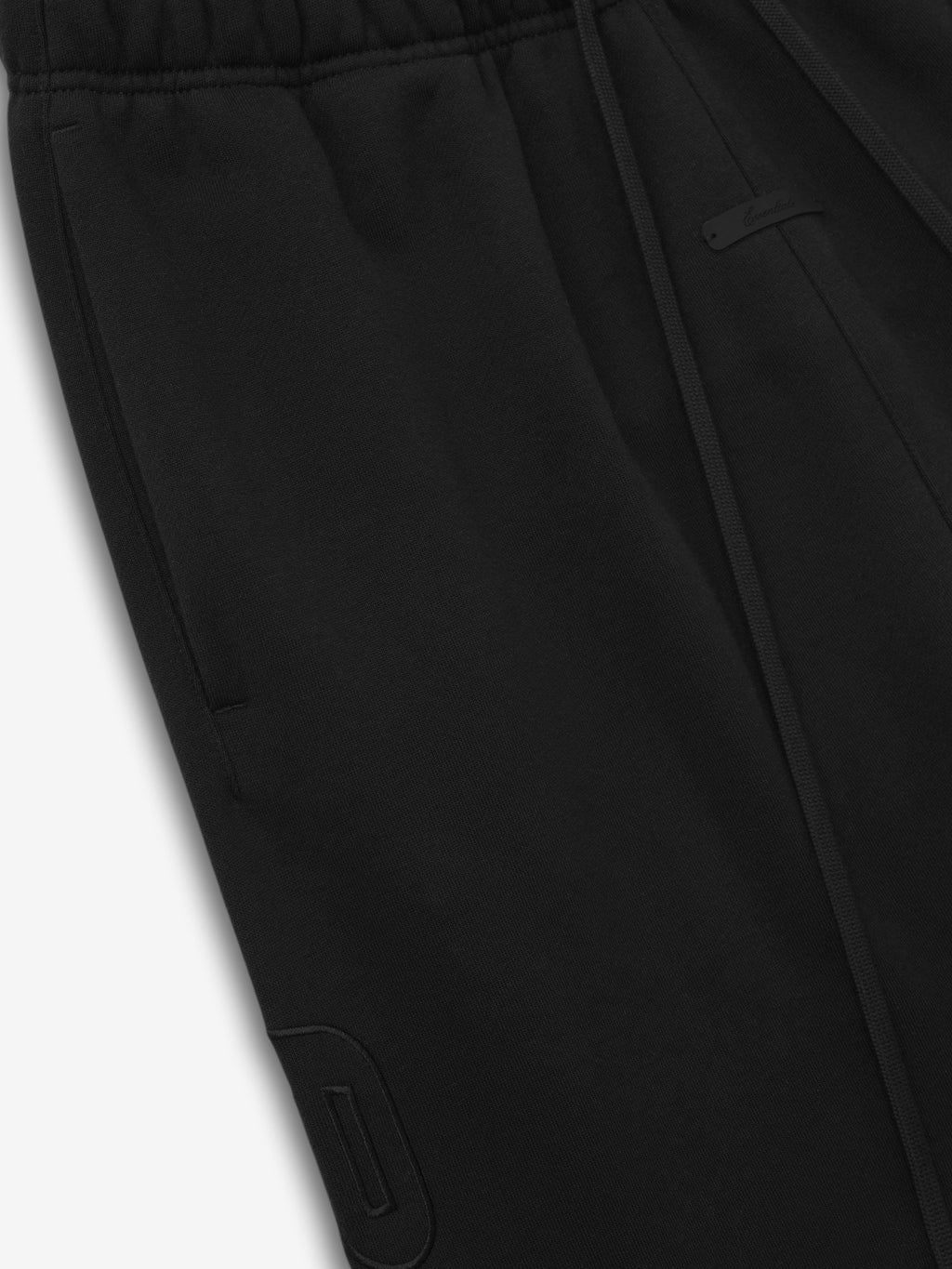 close-up of black baggy sweatpants with elastic waistband, drawstring, and subtle stitched logo detail on leg