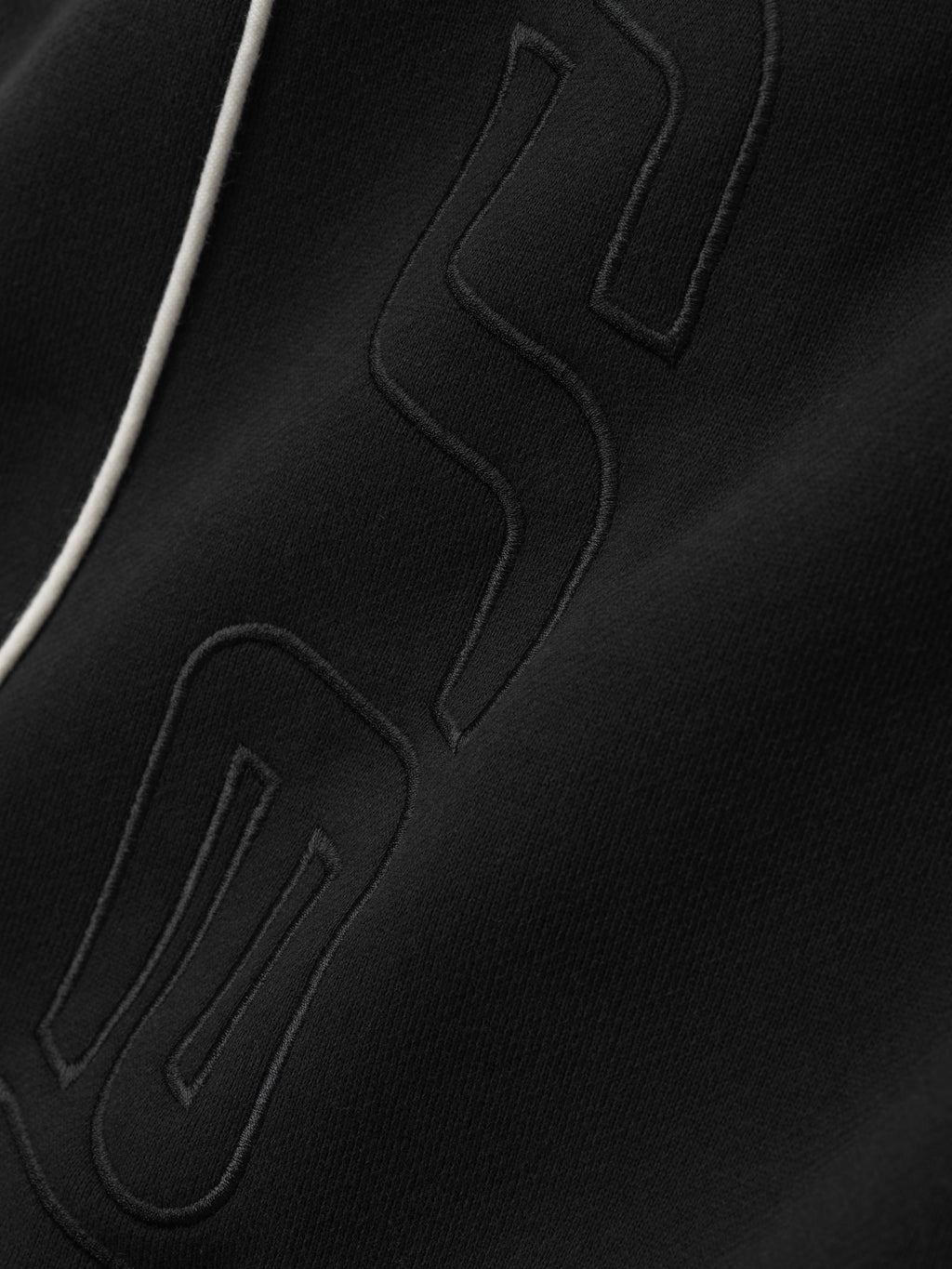 close-up of black core fleece fabric with subtle tonal embroidered Essentials A logo and white sportswear piping detail