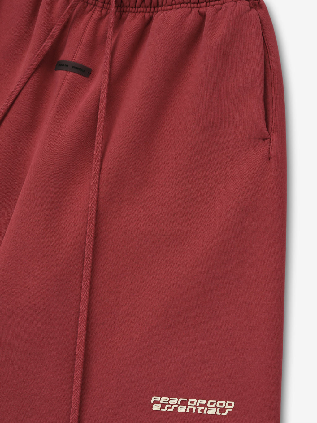Close-up of crimson relaxed sweatshort with elastic waistband, side pocket, long drawstrings, and logo near hem on white background