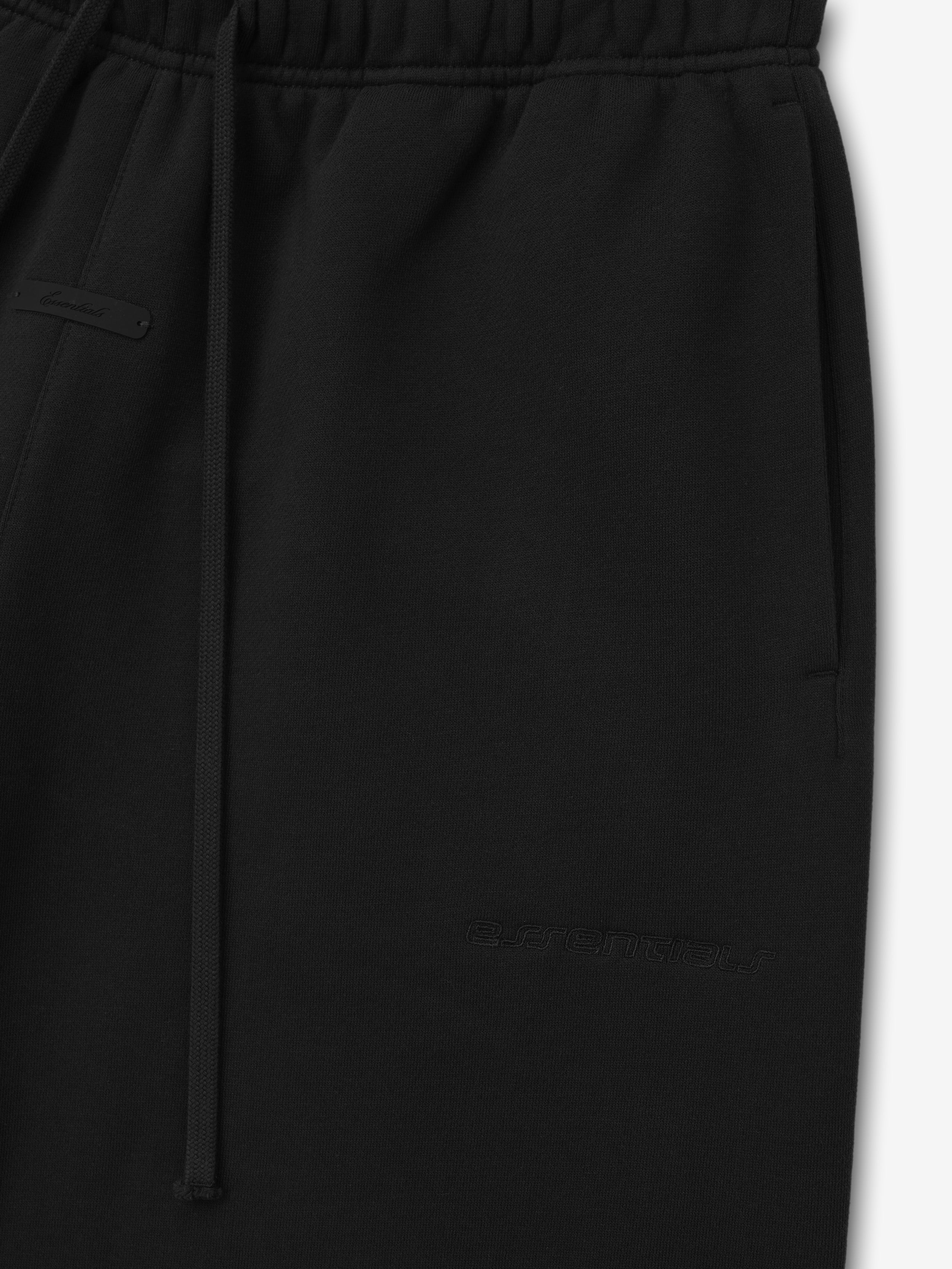 black bonded suede fleece shorts with elongated baggy fit, elastic waistband, drawstring closure, and tonal embossed logo on leg