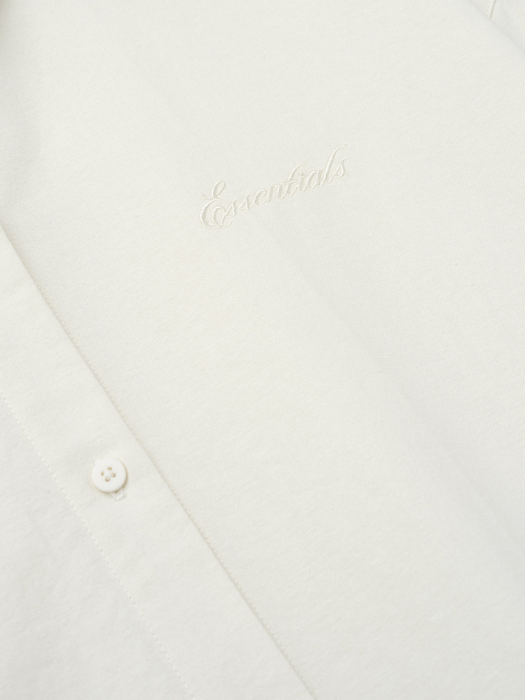 close-up of cream cotton oxford fabric with tonal Essentials embroidery and button detail on womens shirt