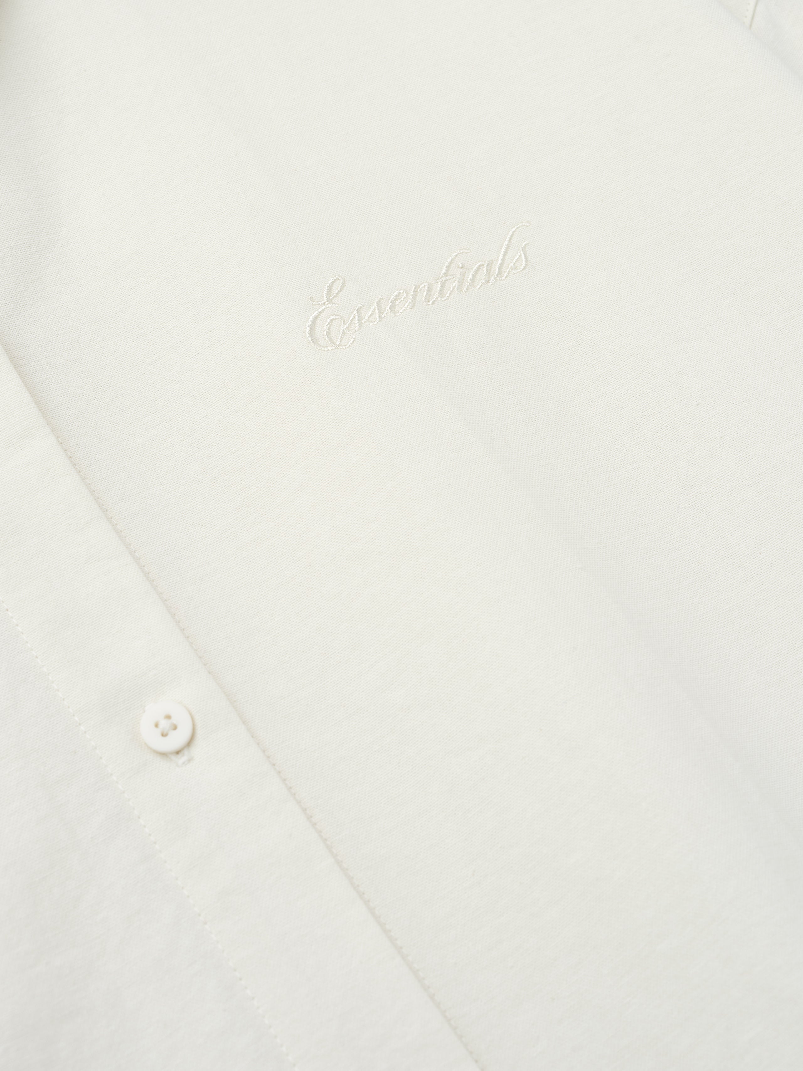 close-up of cream cotton oxford fabric with tonal Essentials embroidery and button detail on womens shirt