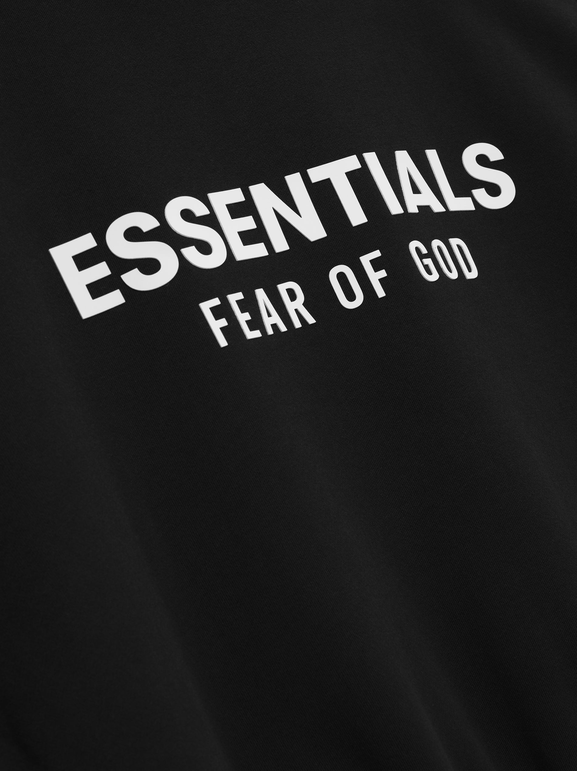 close-up of black heavy fleece hoodie with bold white Essentials Fear of God logo printed on fabric
