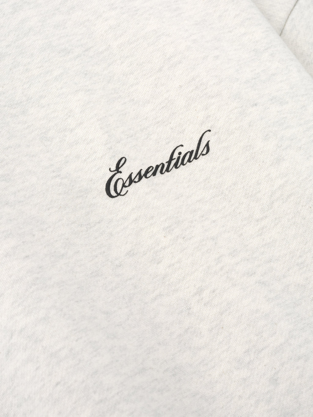 close-up of light cream crewneck sweatshirt fabric with black puff-printed Essentials logo on chest