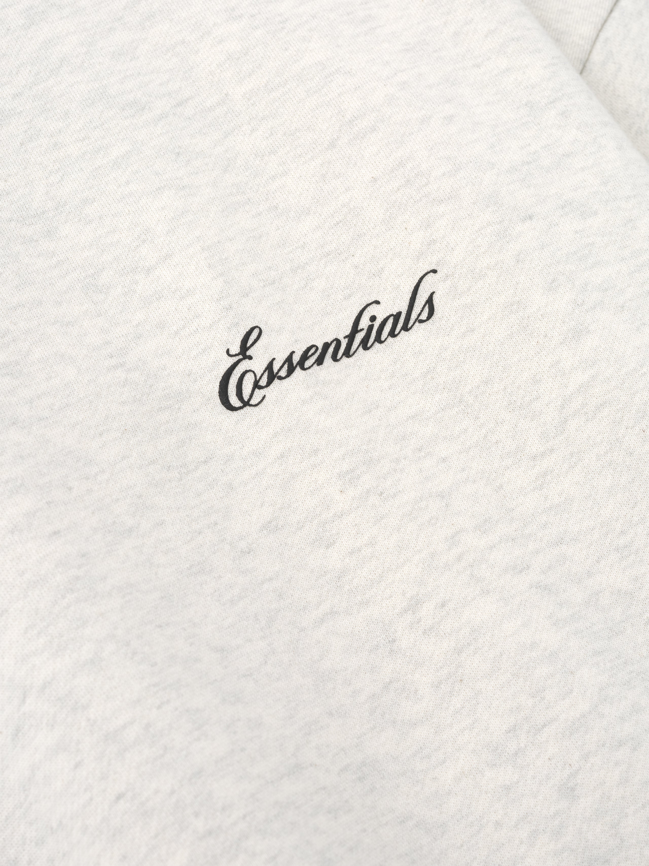 close-up of light cream crewneck sweatshirt fabric with black puff-printed Essentials logo on chest