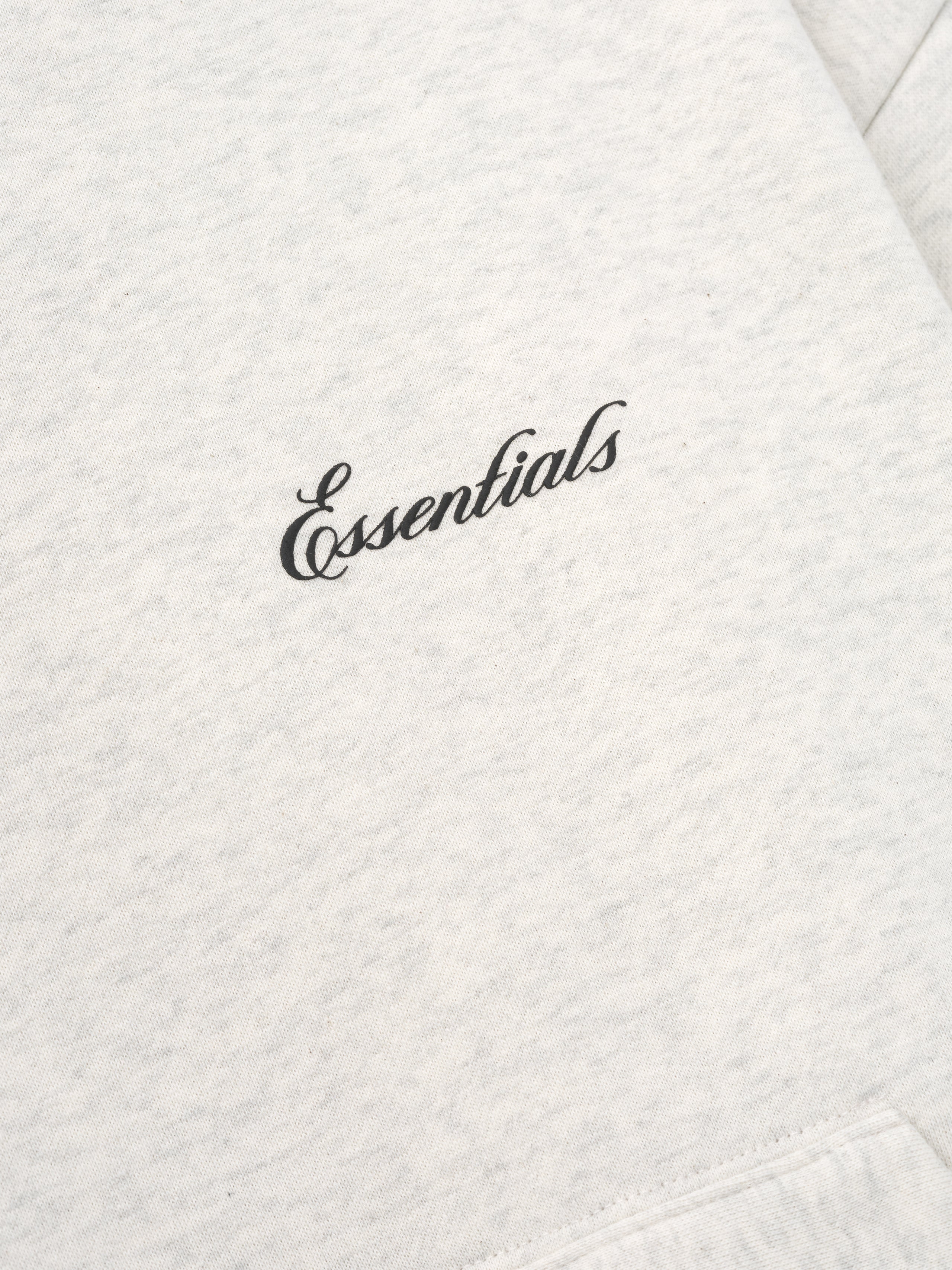 close-up of light heather grey fabric with black puff-printed Essentials signature logo on chest area of hoodie