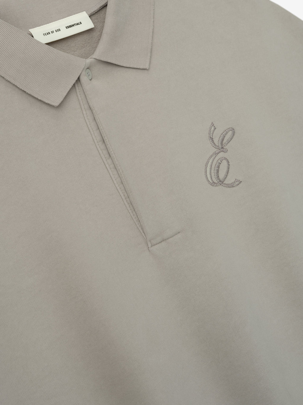Close-up of smoke grey classic polo sweatshirt with embroidered "E" logo near chest and buttoned placket detail