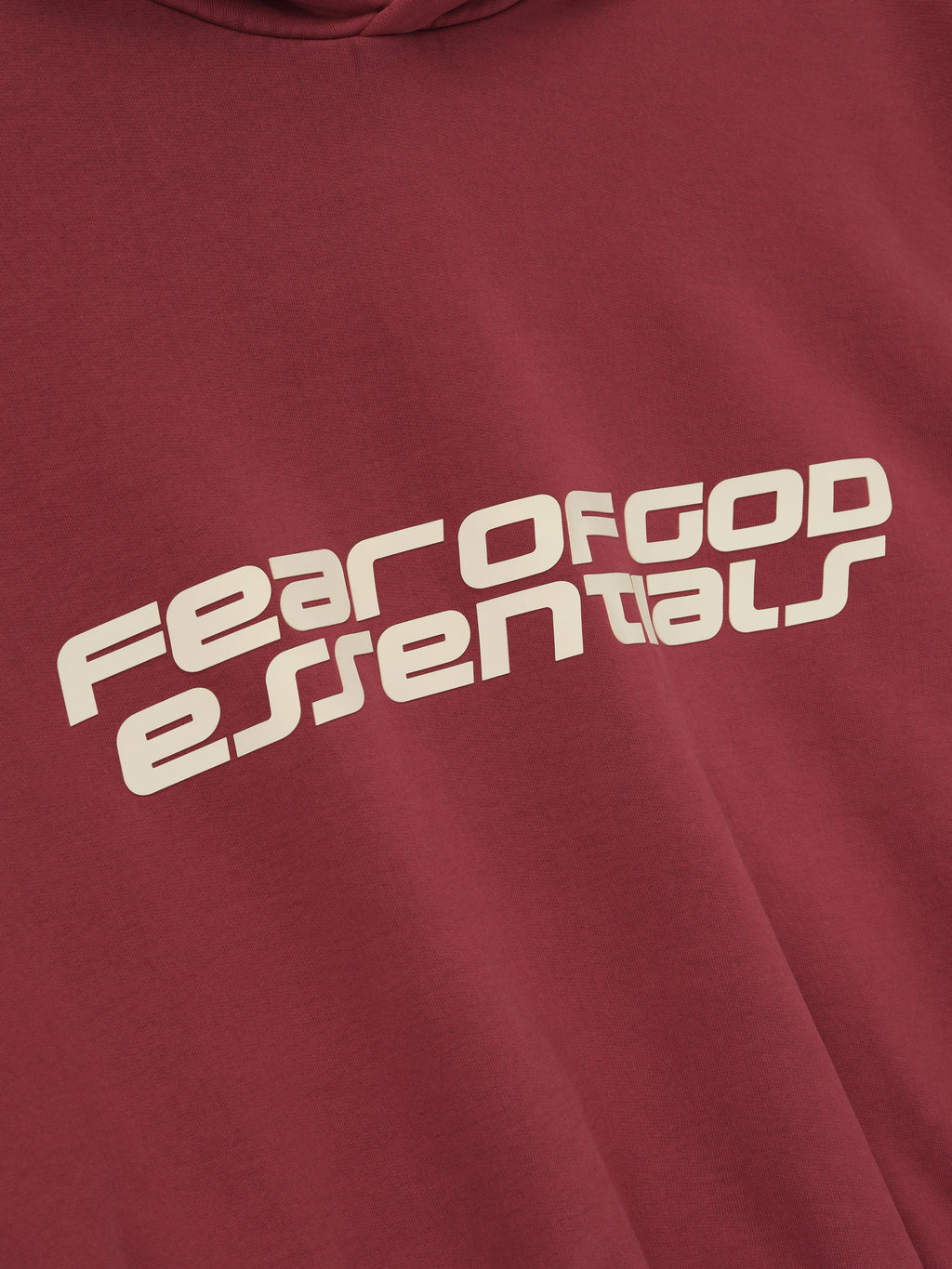 Close-up of crimson cropped relaxed hoodie featuring large slanted Fear of God Essentials logo in cream on front