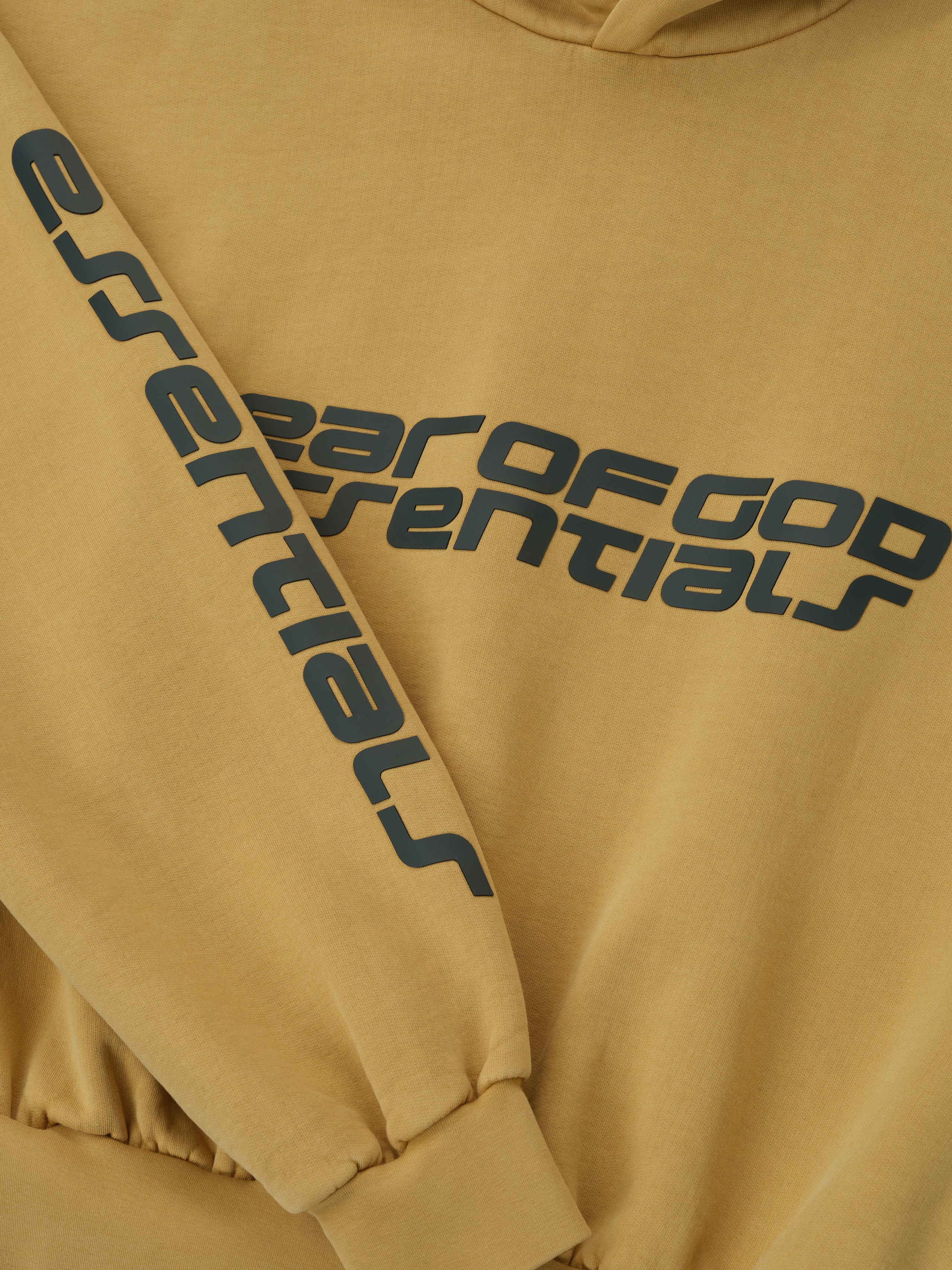 Close-up of canyon-colored cropped relaxed hoodie with black Fear of God Essentials logo on chest and sleeve cuff detail
