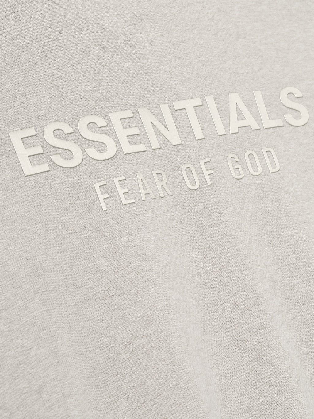 close-up of light beige fleece fabric showing embossed ESSENTIALS Fear of God logo details on front chest area