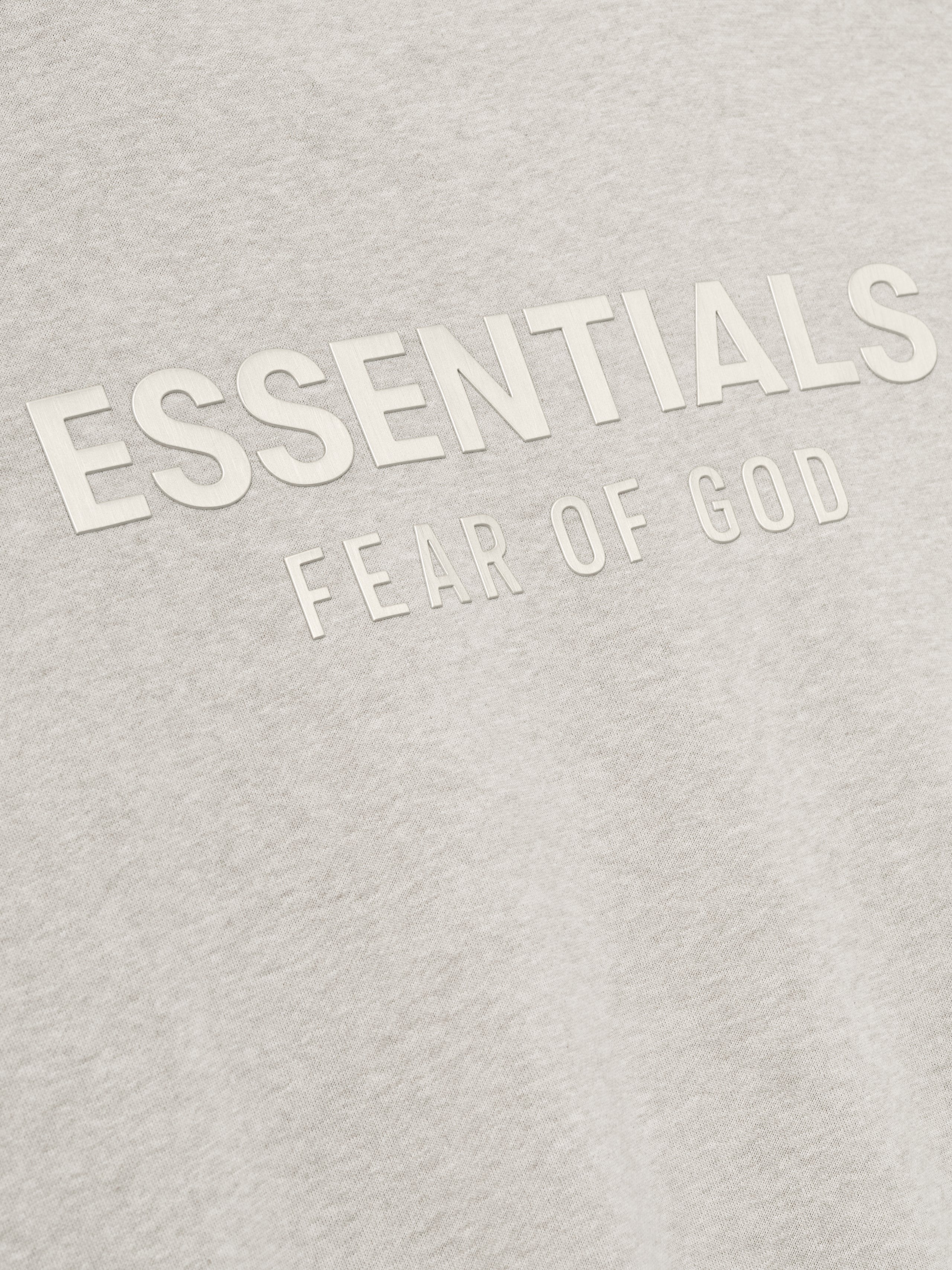 close-up of light beige fleece fabric showing embossed ESSENTIALS Fear of God logo details on front chest area