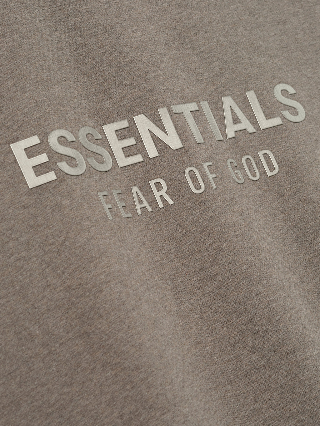 close-up of taupe fleece fabric with embossed ESSENTIALS Fear of God logo on front chest area