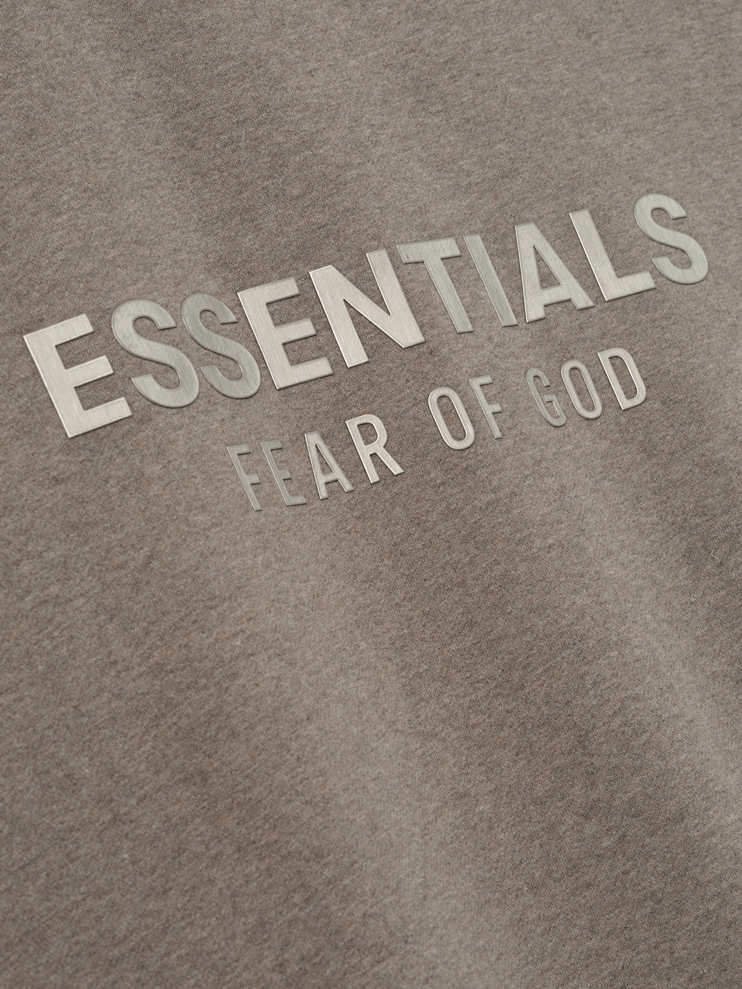 close-up of taupe fleece fabric with embossed ESSENTIALS Fear of God logo on front chest area