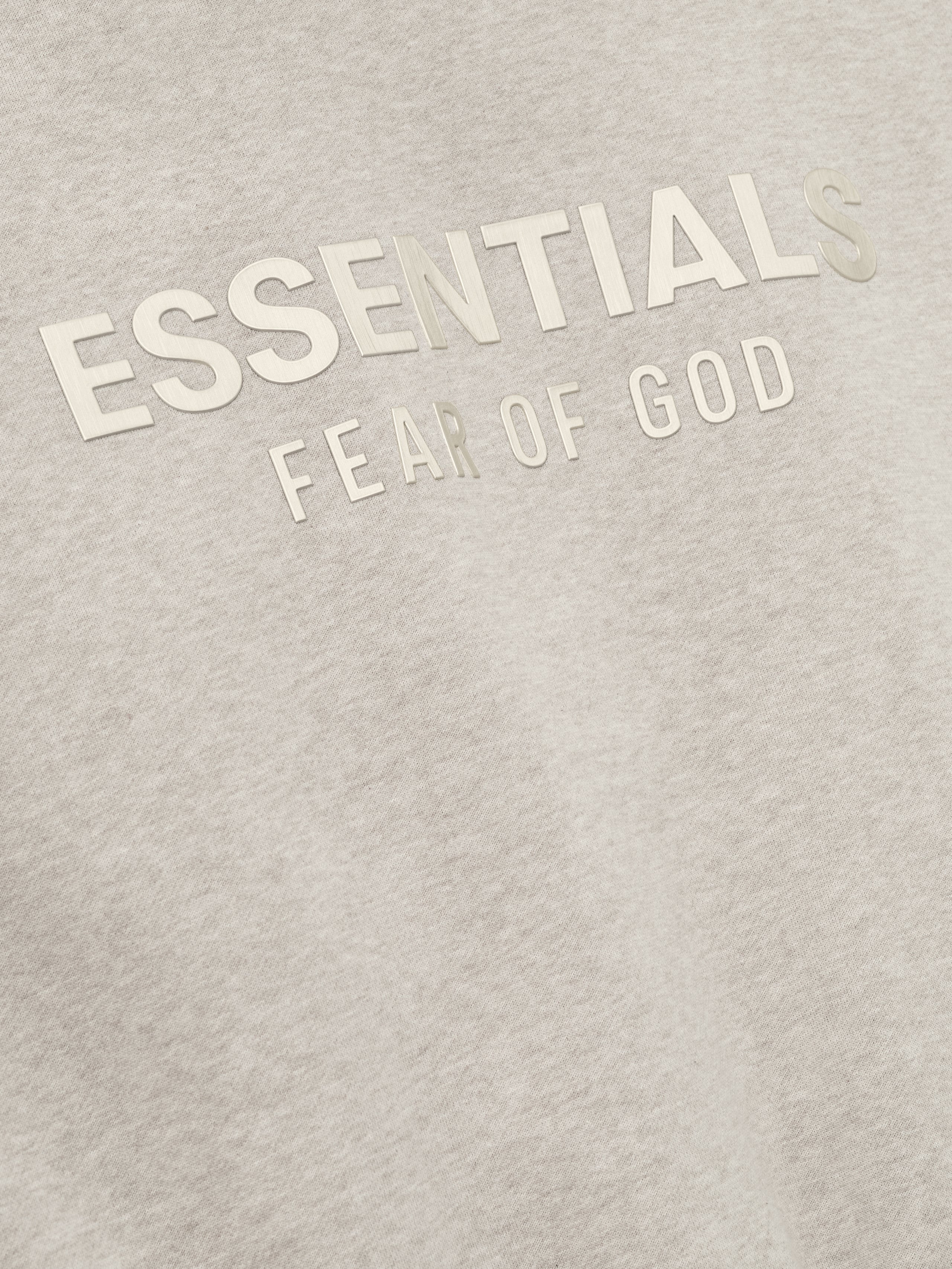 close-up of embossed ESSENTIALS Fear of God logo on soft light beige fleece fabric of classic hoodie