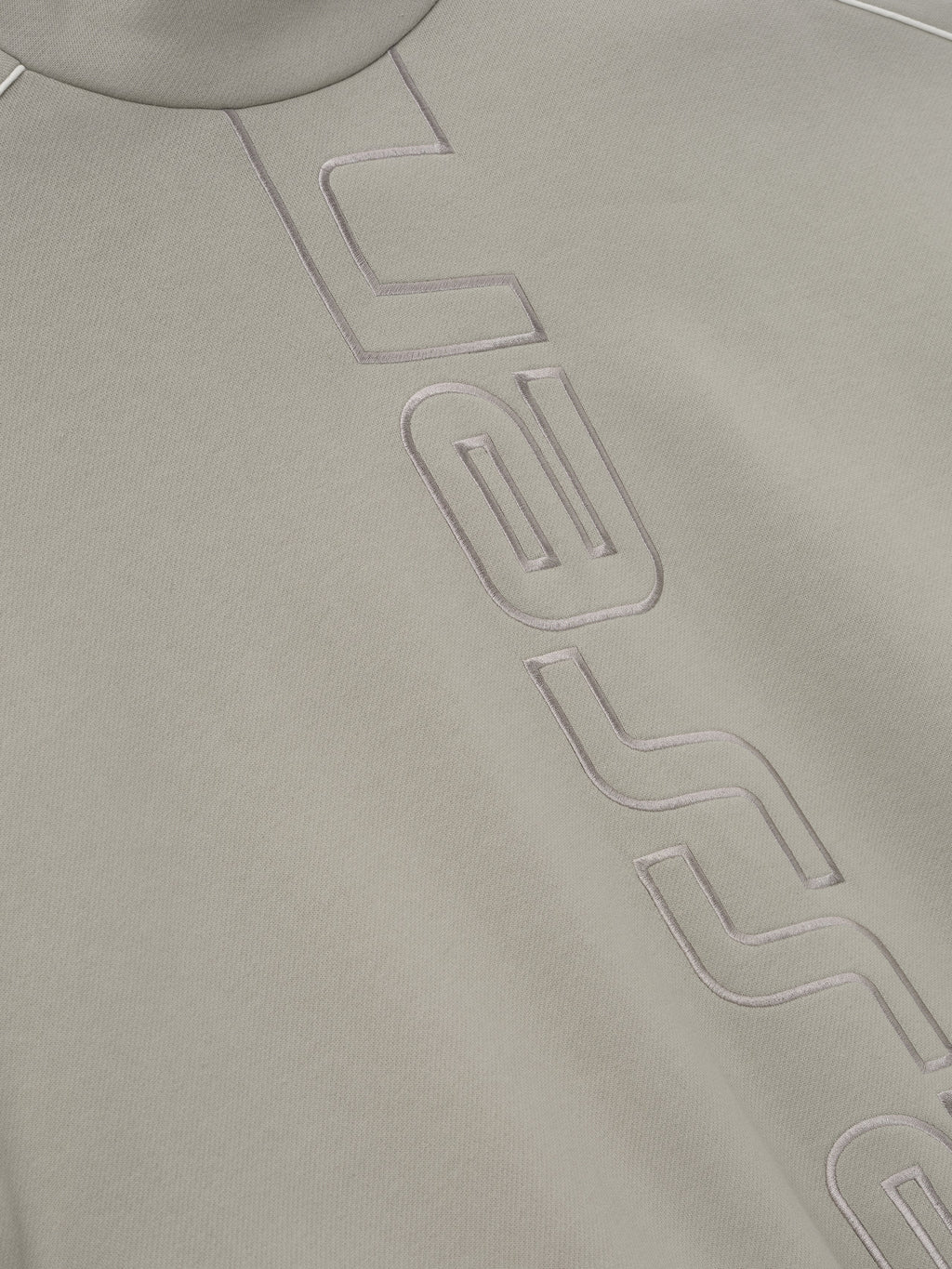 close-up of light beige fleece fabric with raised stitched Essentials Active Trace logo detailing