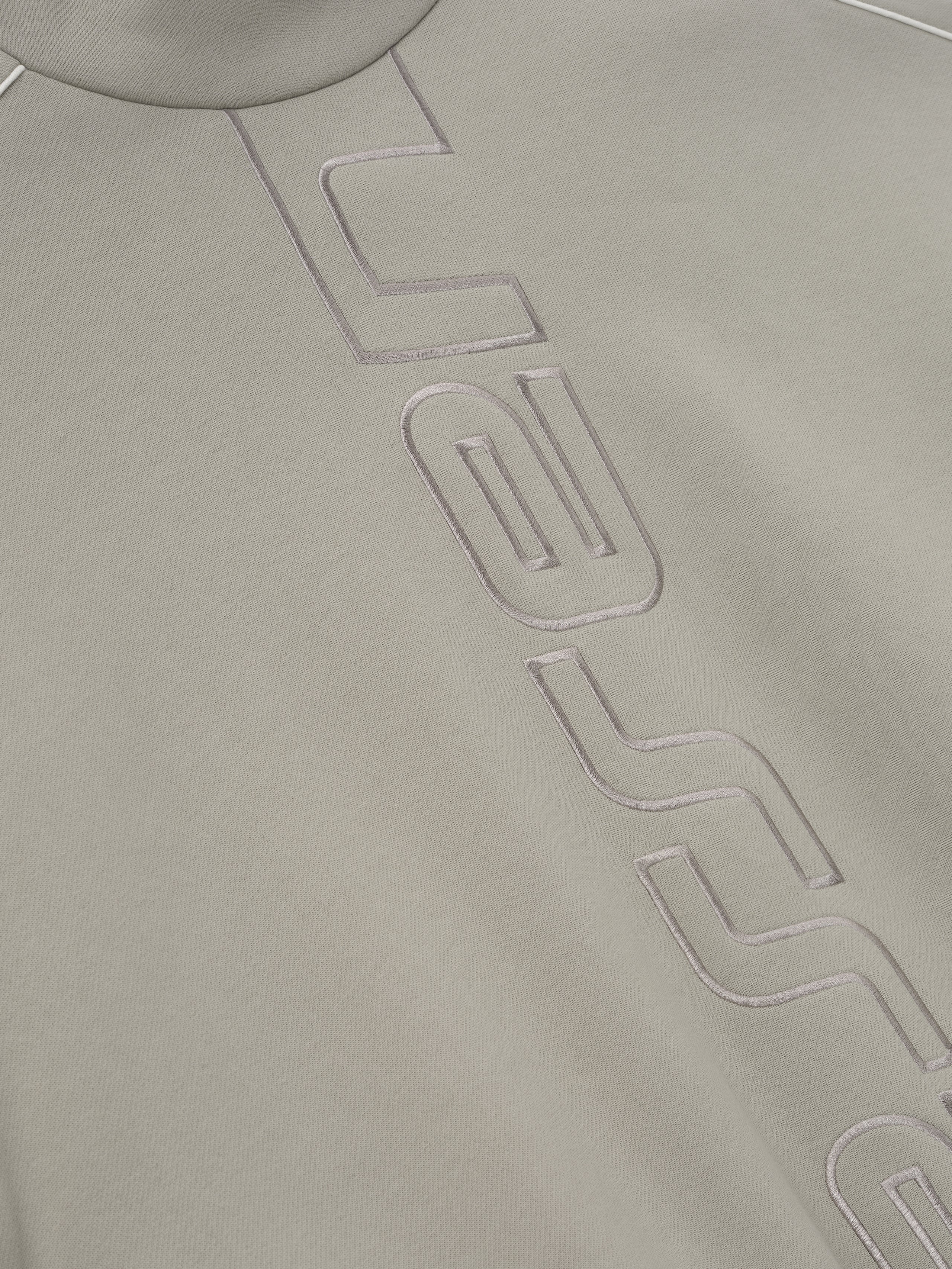 close-up of light beige fleece fabric with raised stitched Essentials Active Trace logo detailing