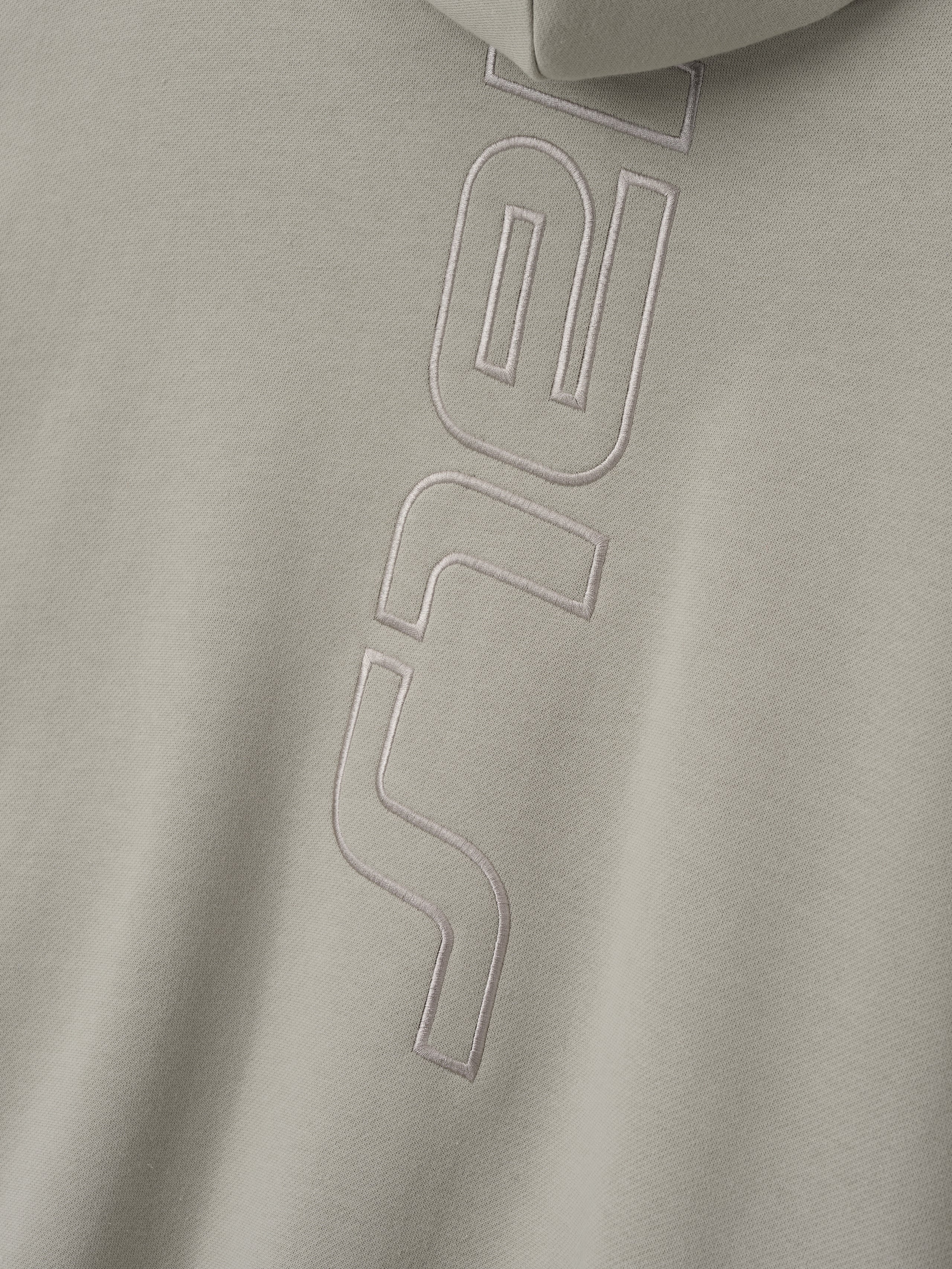 close-up of beige fleece fabric with raised stitched vertical Active Trace logo detail on hoodie back