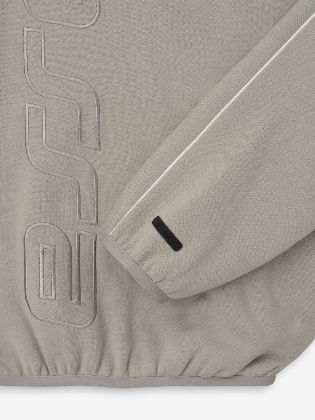 Close-up of light taupe sweatshirt sleeve with white piping and tonal embossed lettering on the body