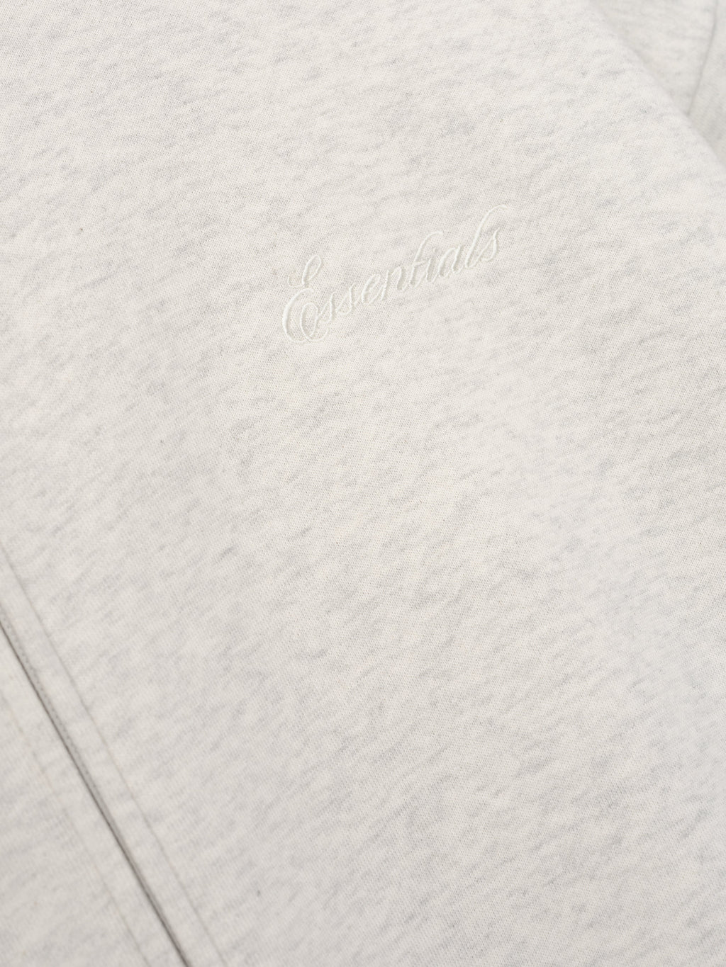 close-up of light gray core fleece fabric with white embroidered Essentials signature logo on front panel
