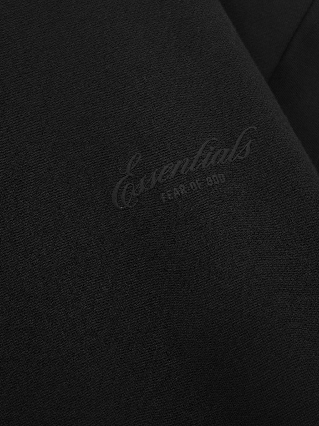 close-up of black fleece fabric with embossed Essentials Fear of God logo on chest panel of sweatshirt