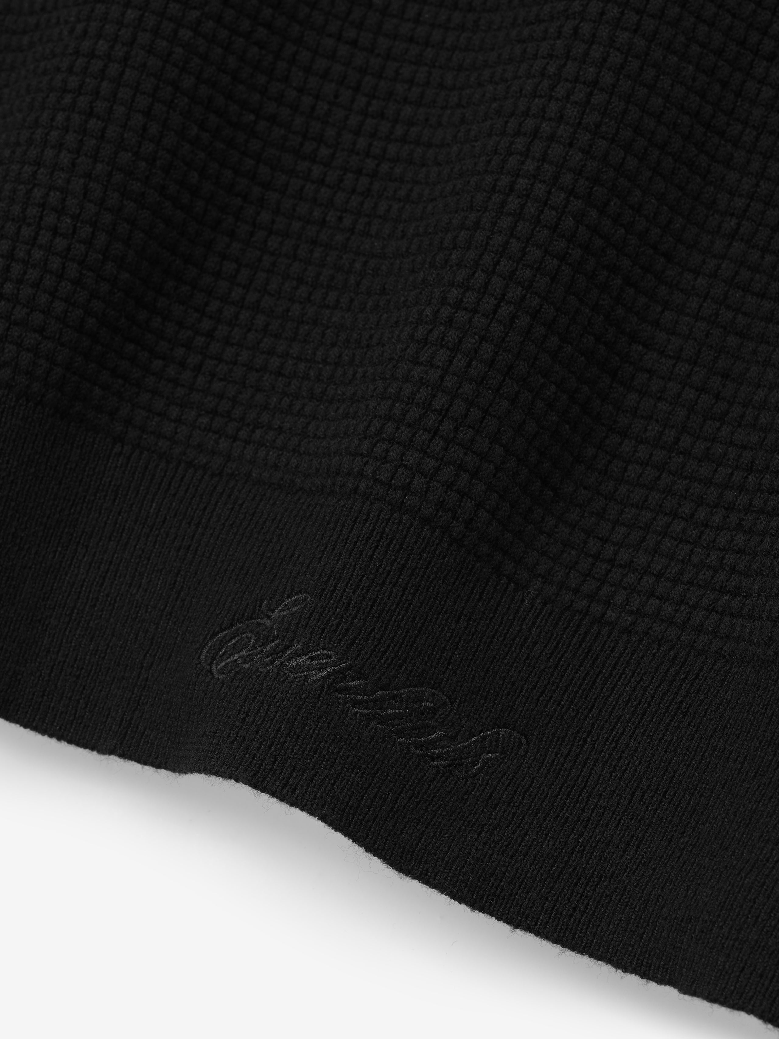 Close-up of a black textured fabric with a brand logo in cursive saying "Essentials" on a white background
