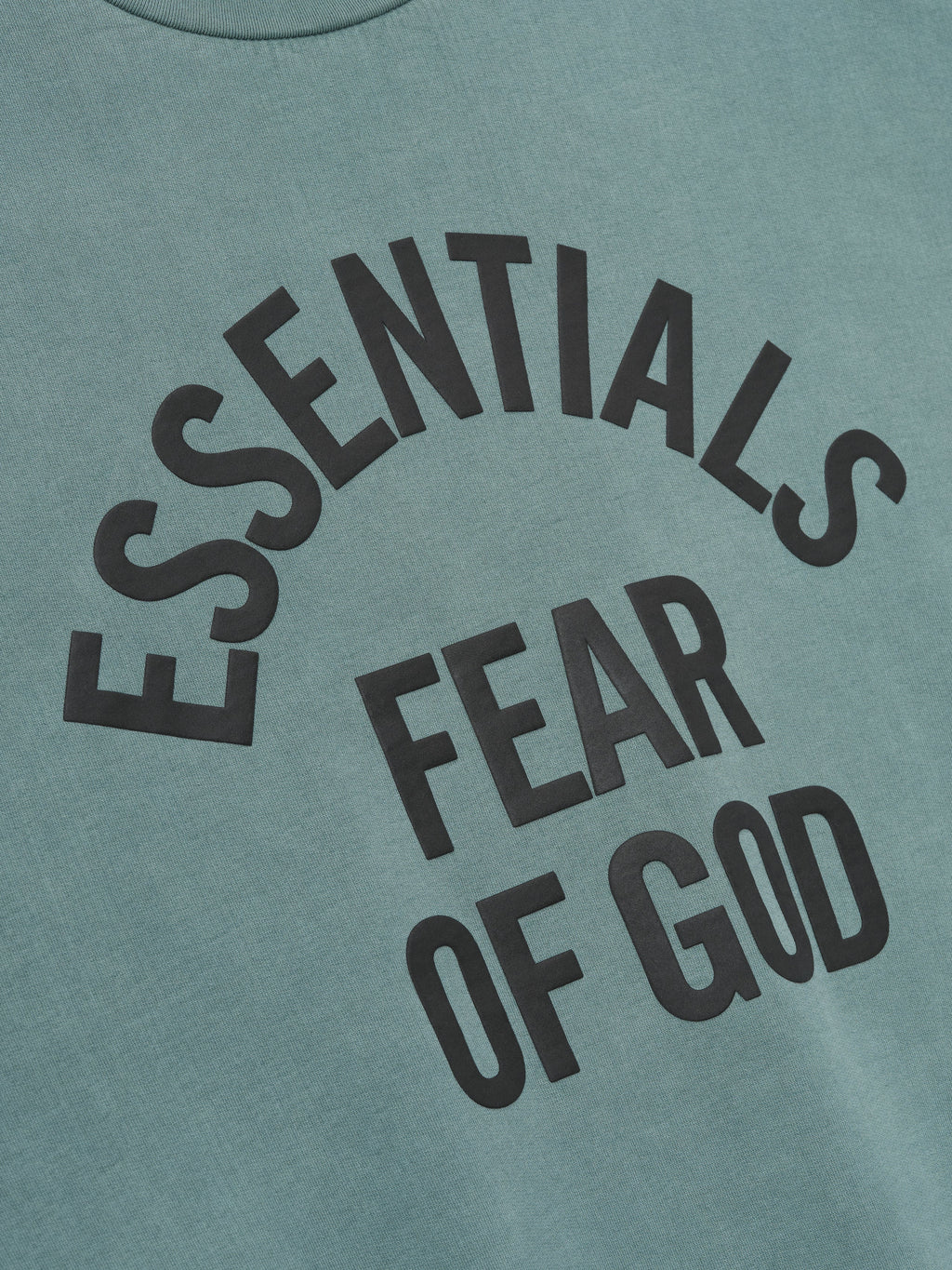 close-up of pigment-dyed teal fabric with large black Essentials Fear of God printed logo on sweatshirt