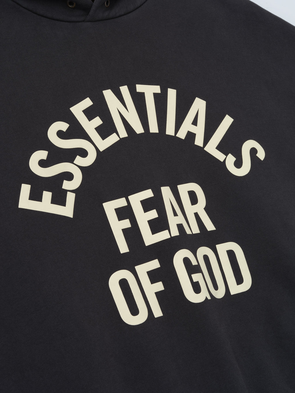 close-up of black pigment-dyed hoodie with cream Essentials Fear of God arched logo print on chest