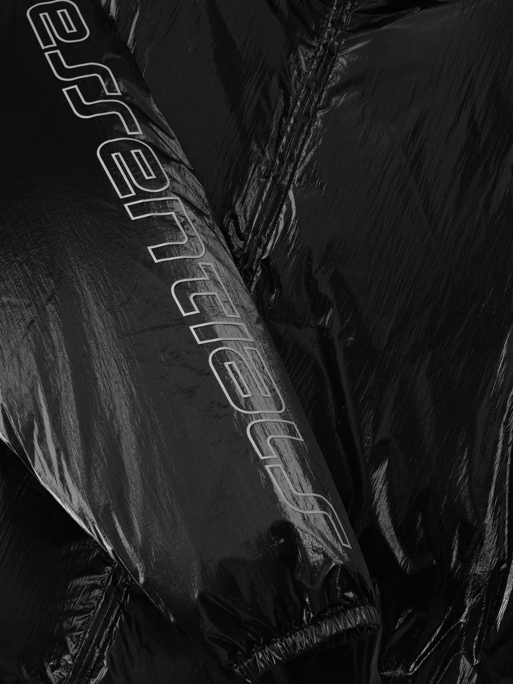 Close-up of shiny metallic black ripstop nylon puffer jacket sleeve with large Essentials logo, file 202HO258181F, gallery 0