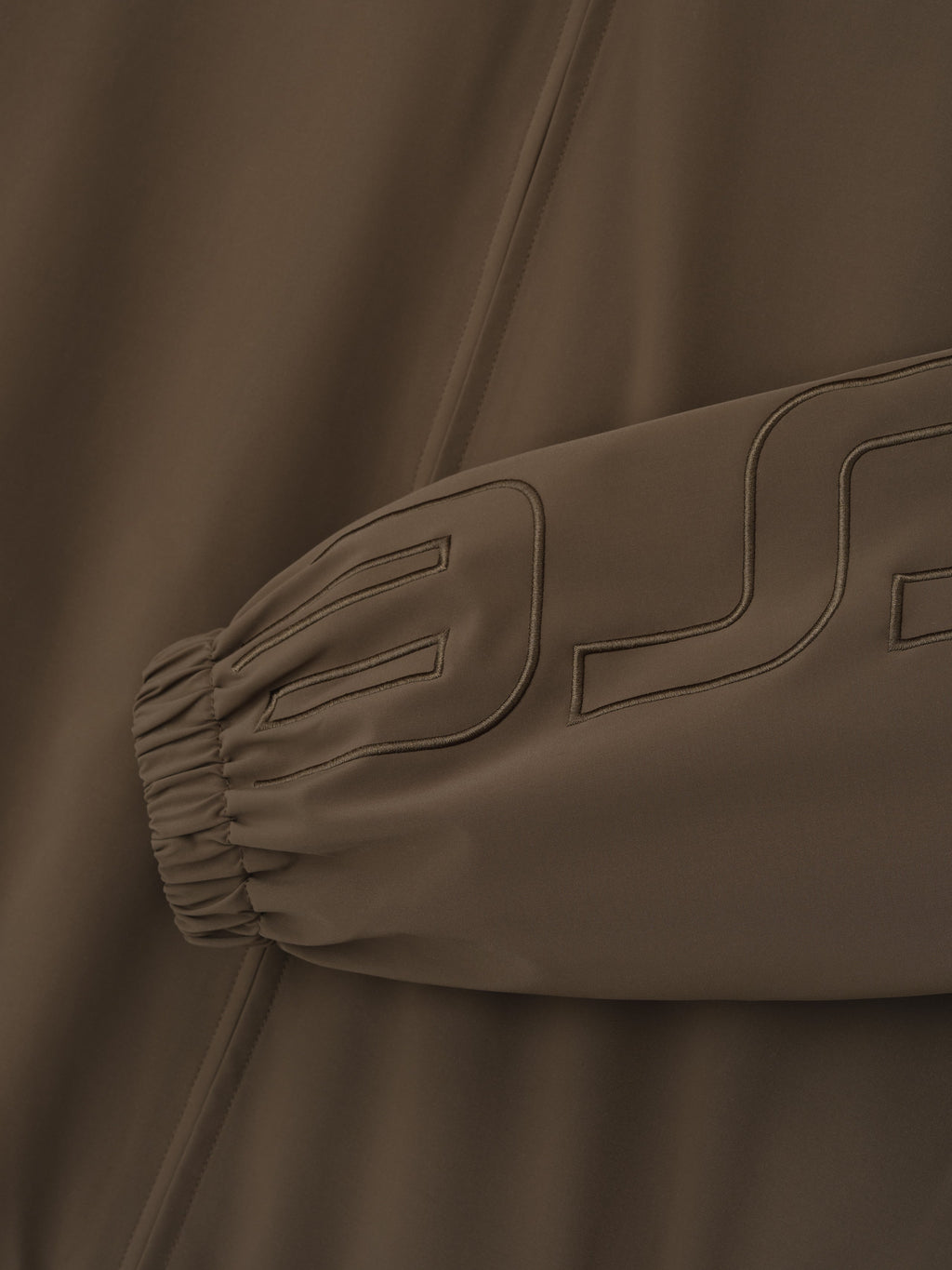 close-up of brown track jacket sleeve with elastic cuff and tonal stitched logo detail on sportswear fabric