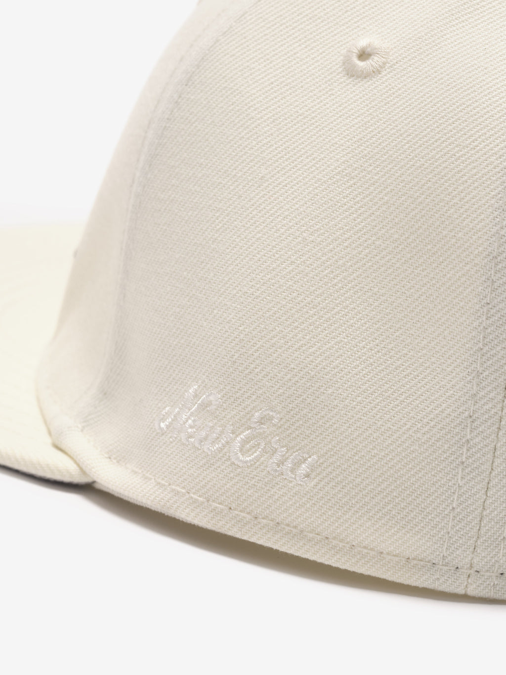close-up of off-white snapback cap front panel with subtle embroidered Fear of God logo on textured fabric