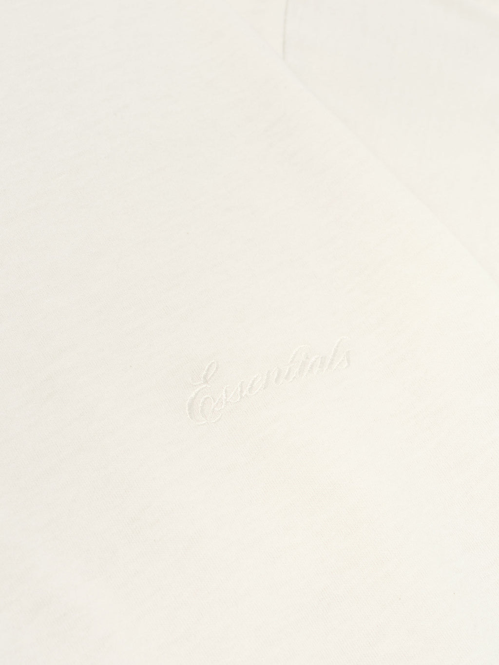 Close-up of ivory Kids Embroidered Essential Tee showing subtle tonal Essentials script on fabric, gallery position 0, file 785HO251462K_KIDS_ESSENTIAL_TEE-IVORY_3.jpg