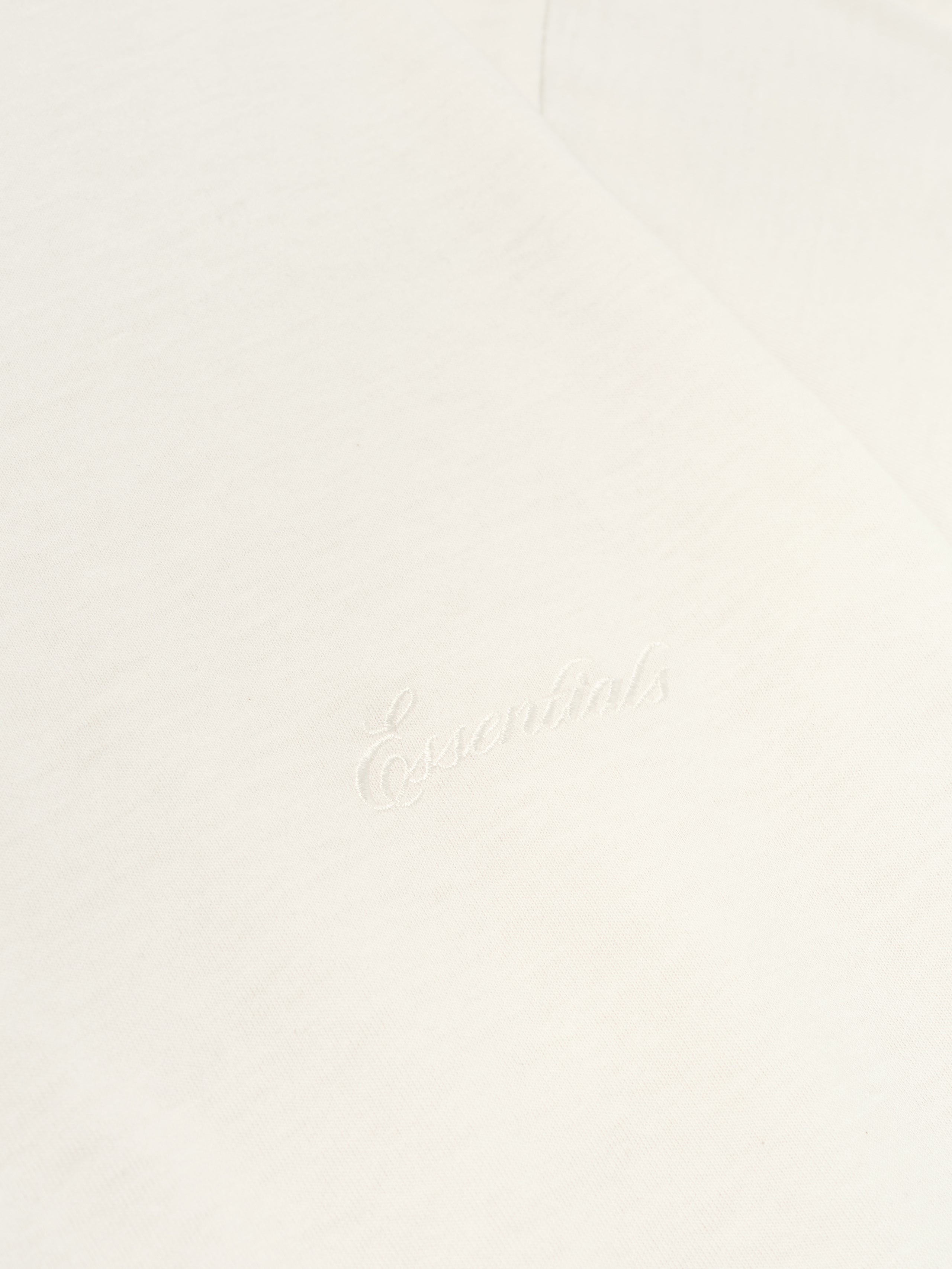 Close-up of ivory Kids Embroidered Essential Tee showing subtle tonal Essentials script on fabric, gallery position 0, file 785HO251462K_KIDS_ESSENTIAL_TEE-IVORY_3.jpg