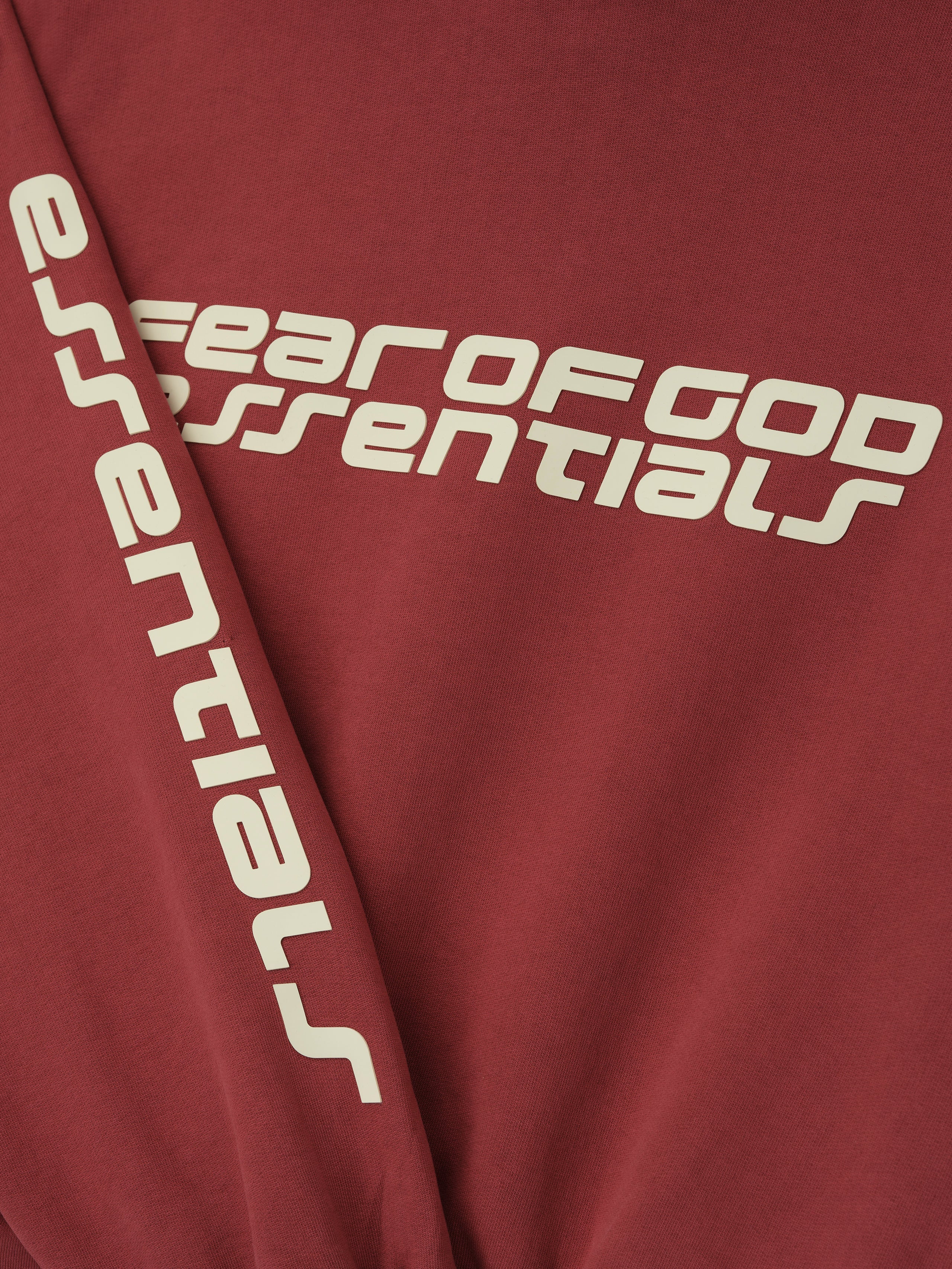 Close-up of crimson Kids Classic Hoodie showing Fear of God Essentials logo across chest and down sleeve, gallery position 0