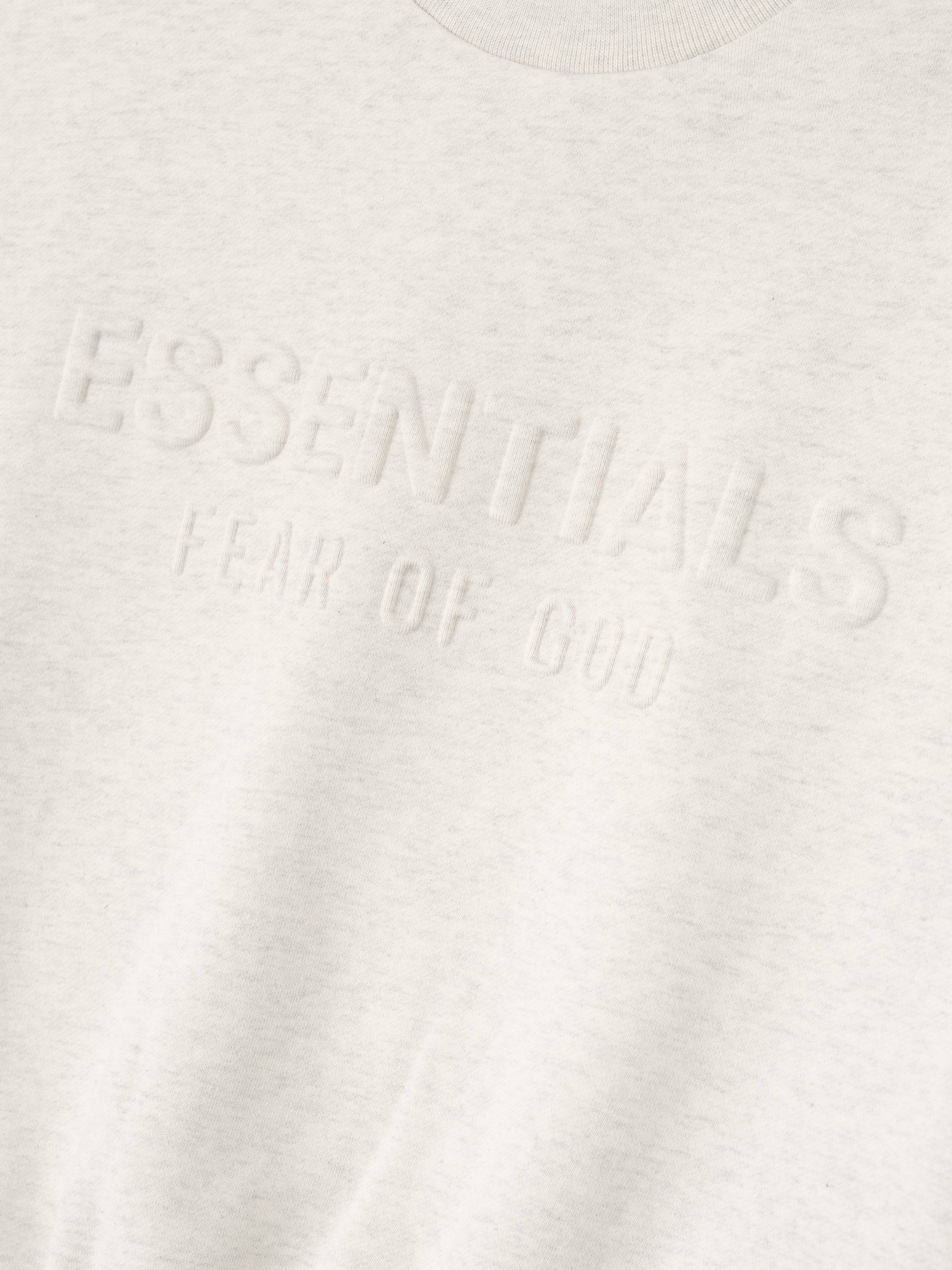 Close-up of oatmeal heather kids sweatshirt showing embossed ESSENTIALS fear of God logo on soft fabric, gallery position 0