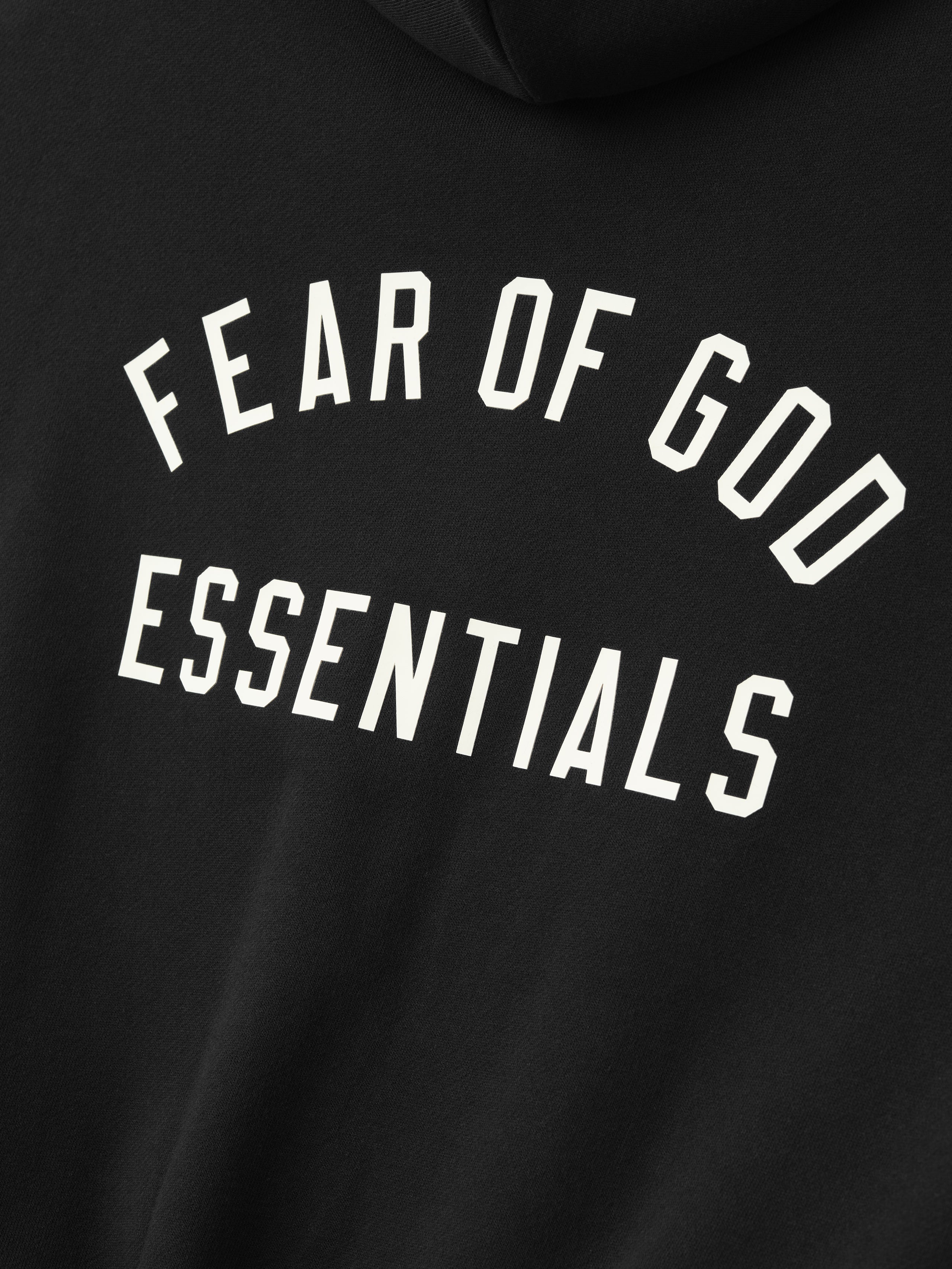 close-up of black kids hoodie with arched Fear of God Essentials logo printed in bold white text on back