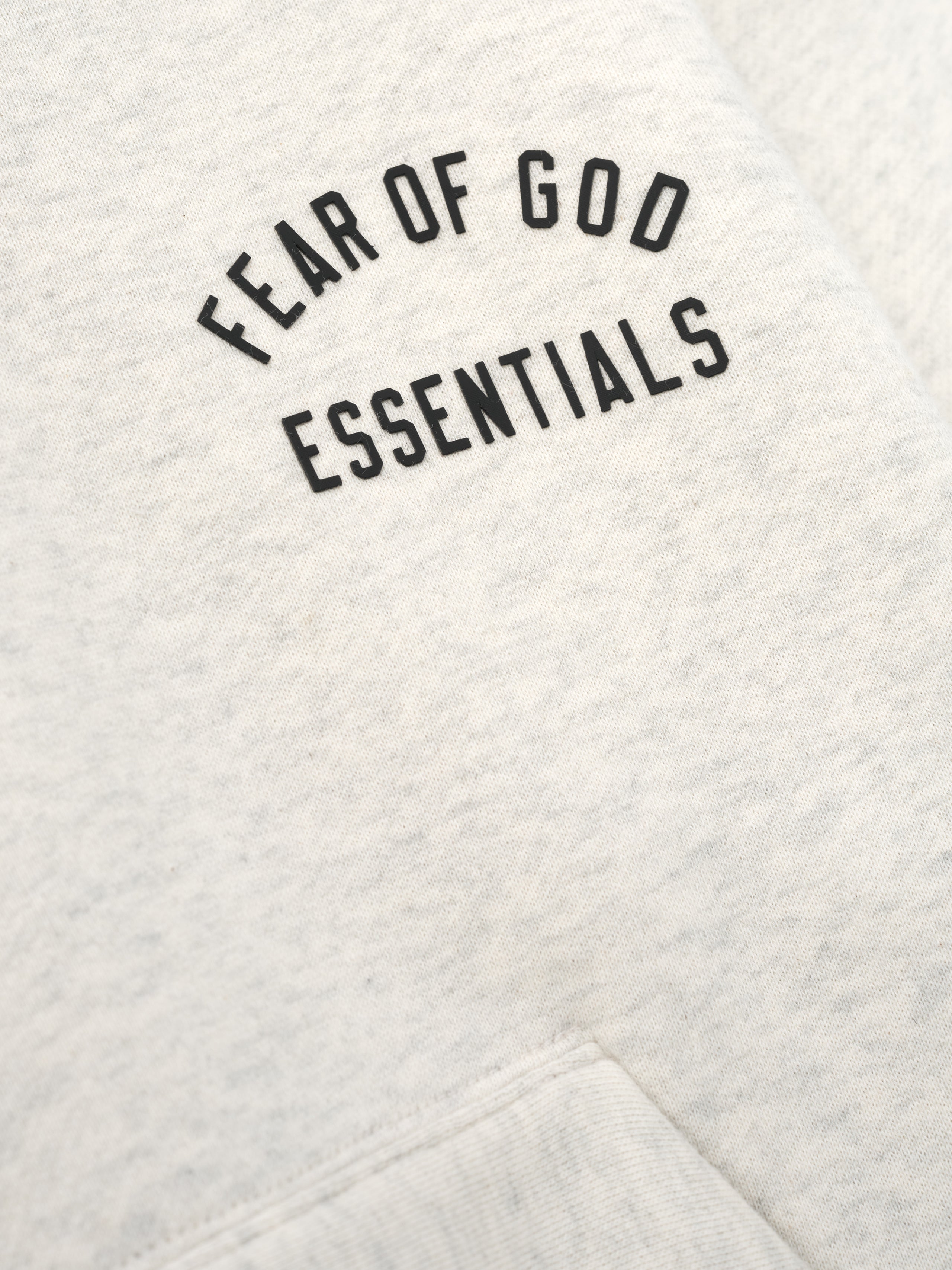 close-up of light beige kids hoodie fabric with Fear of God Essentials logo printed on chest in black text