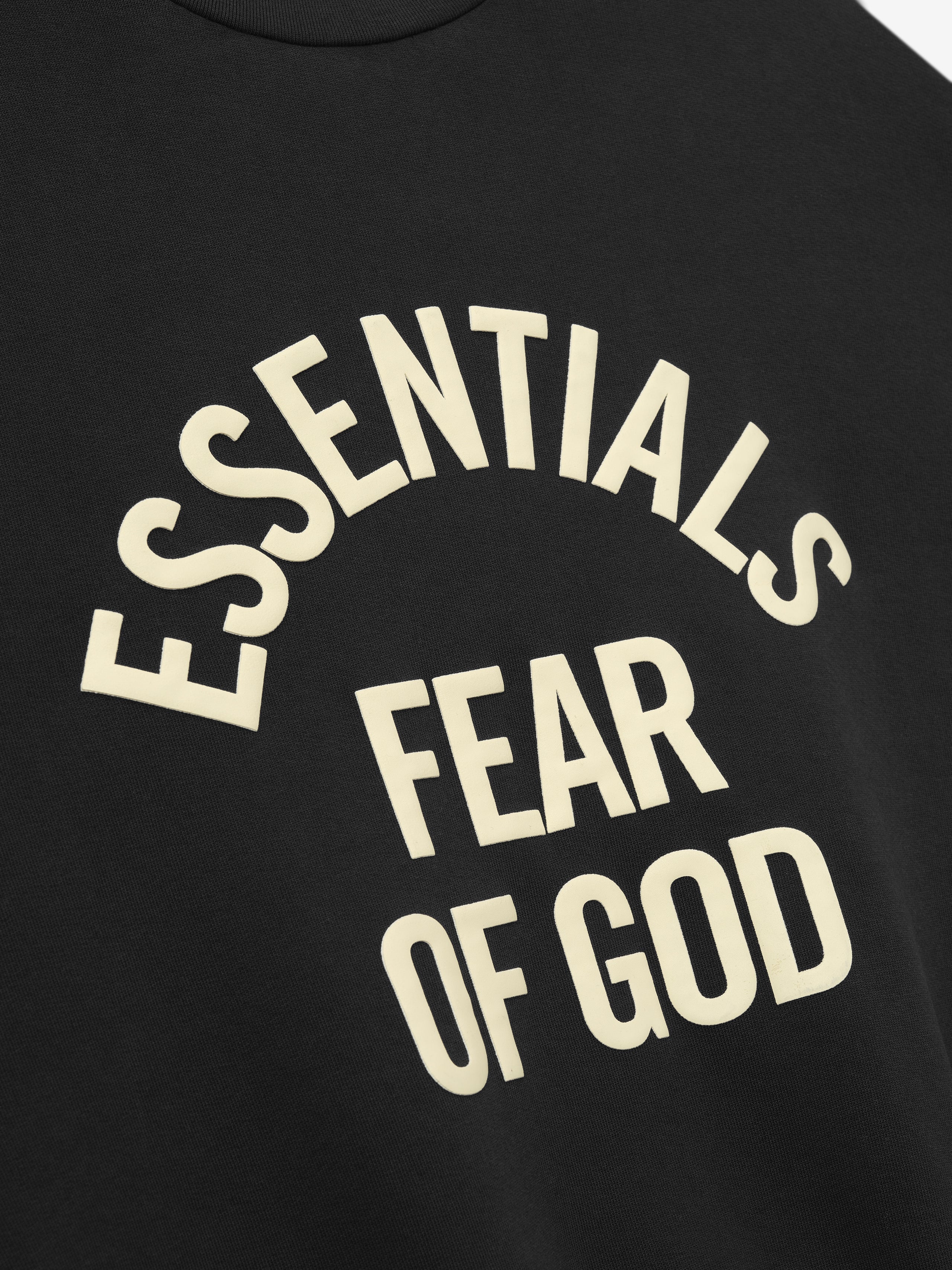 close-up of black crewneck sweatshirt with arched Essentials Fear of God logo printed in cream text on front