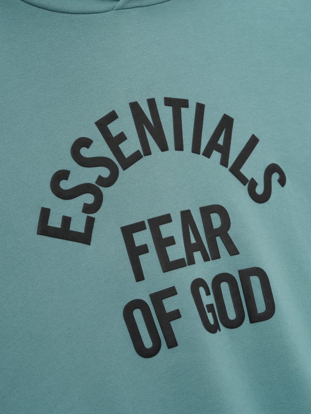 close-up of teal Kids Campus 90s hoodie showing black Essentials Fear of God text in curved layout on cotton fleece fabric