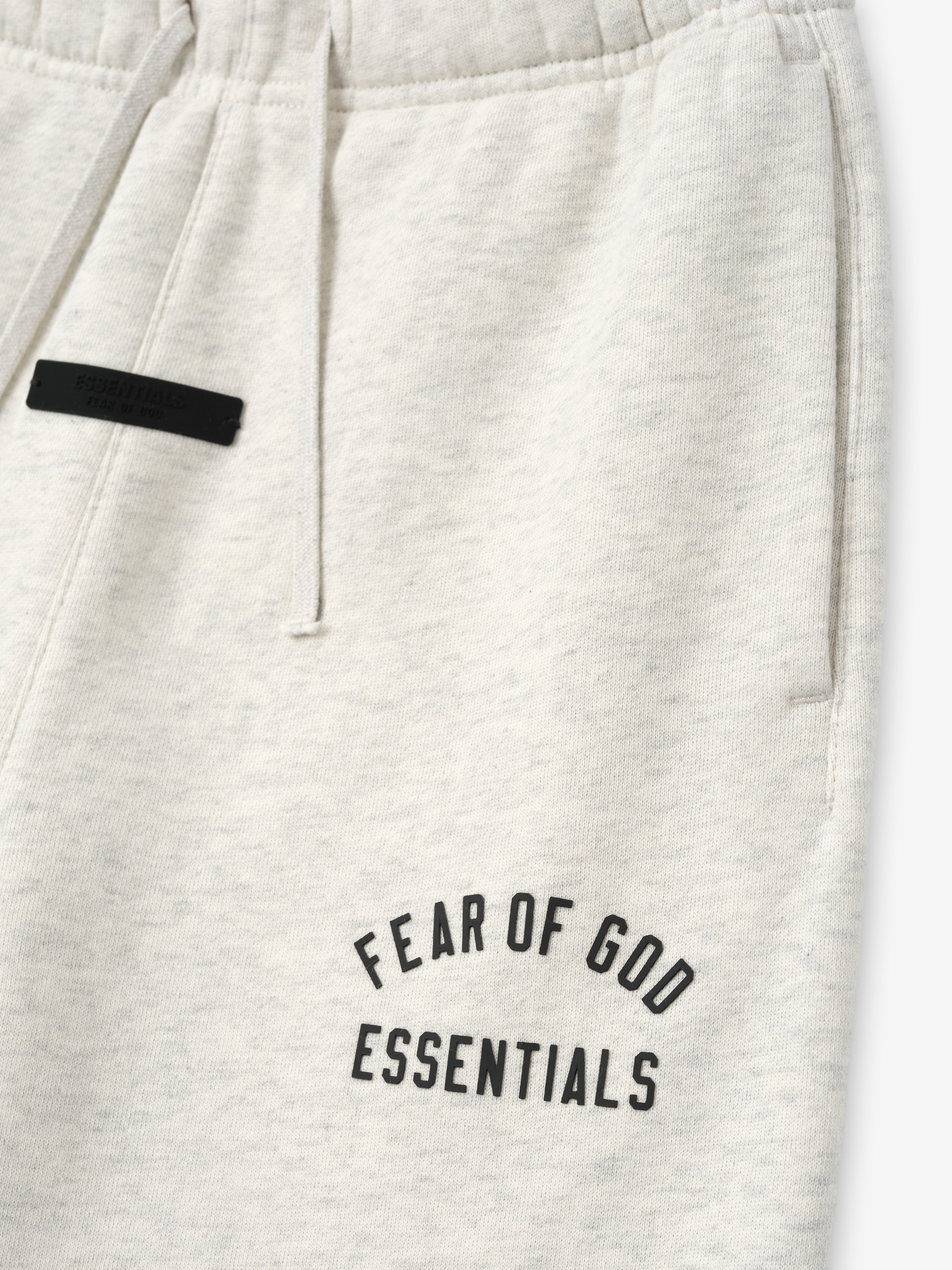 close-up of off-white kids sweatpant featuring black Fear of God Essentials text and drawstring waistband