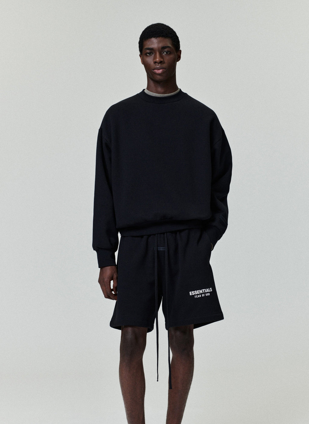 Black classic sweatshorts with adjustable drawstring, side pockets, and white "ESSENTIALS FEAR OF GOD" logo on left leg