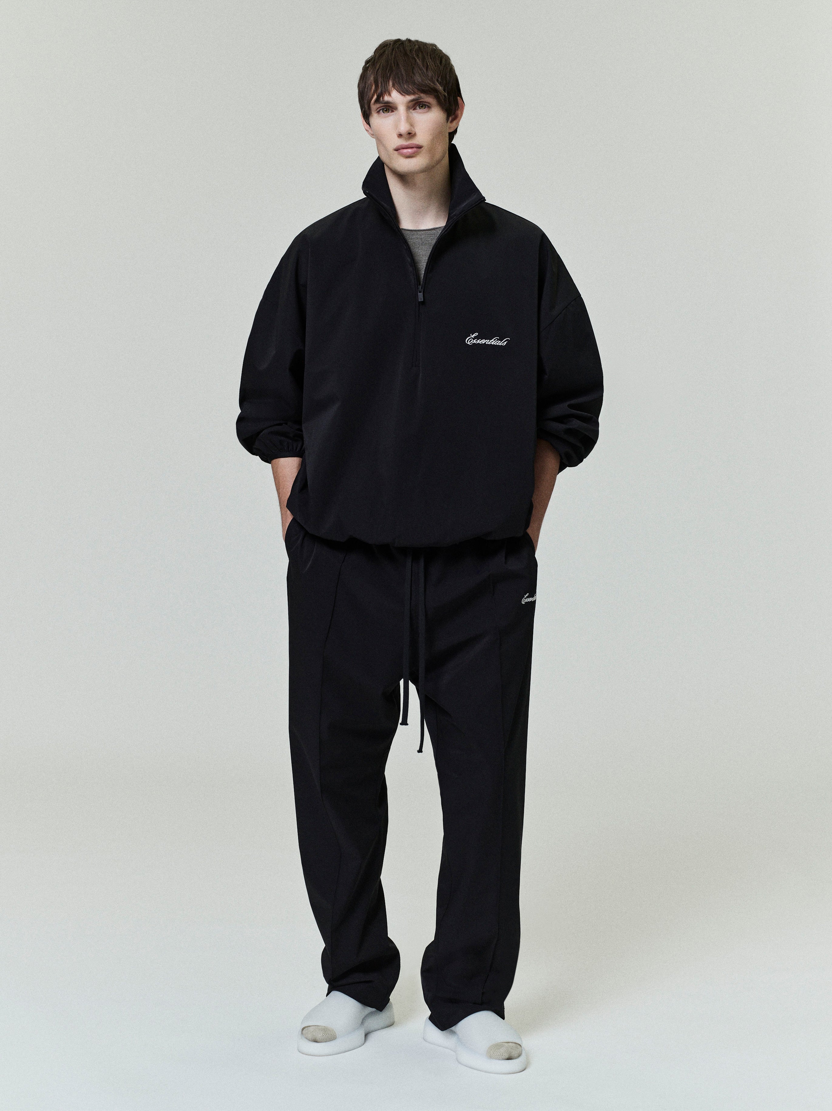 Front view of model wearing black Sporty Nylon Half Zip with matching pants and white slides on plain background