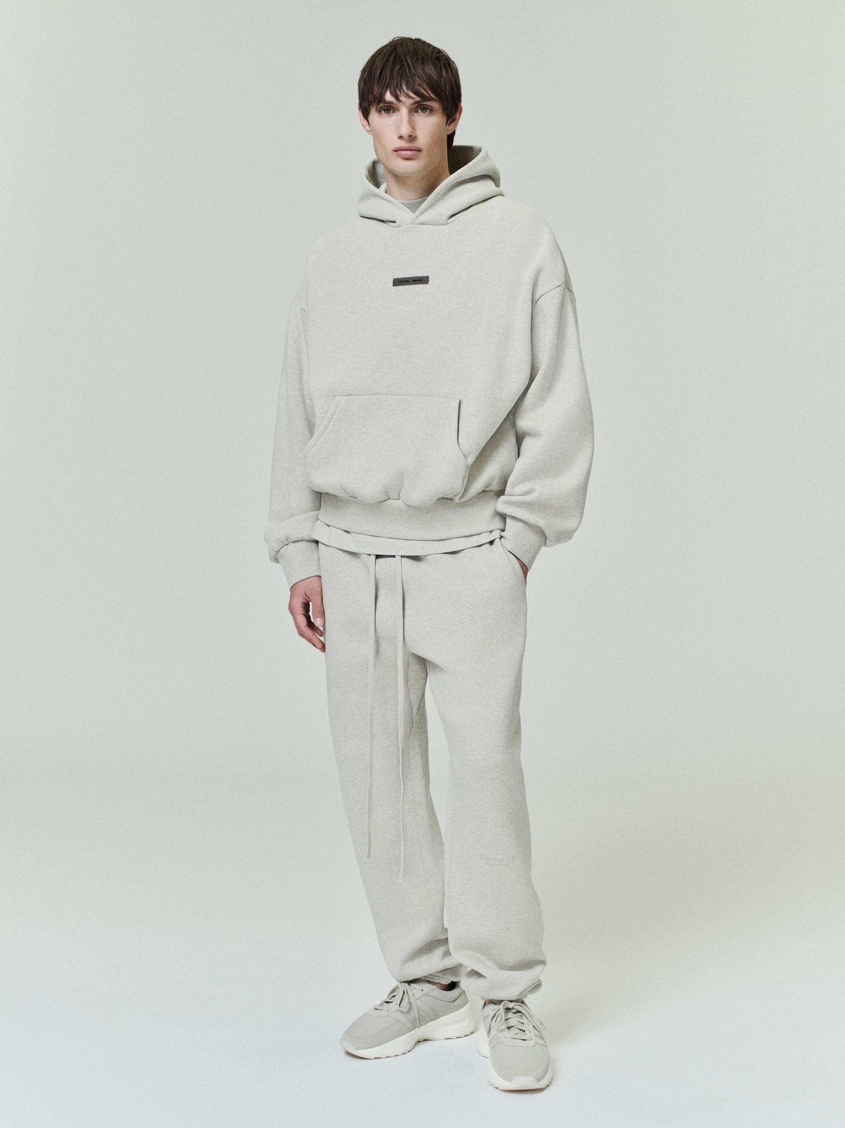 male model wearing oversized off-white fleece hoodie with front kangaroo pocket and relaxed fit with matching sweatpants