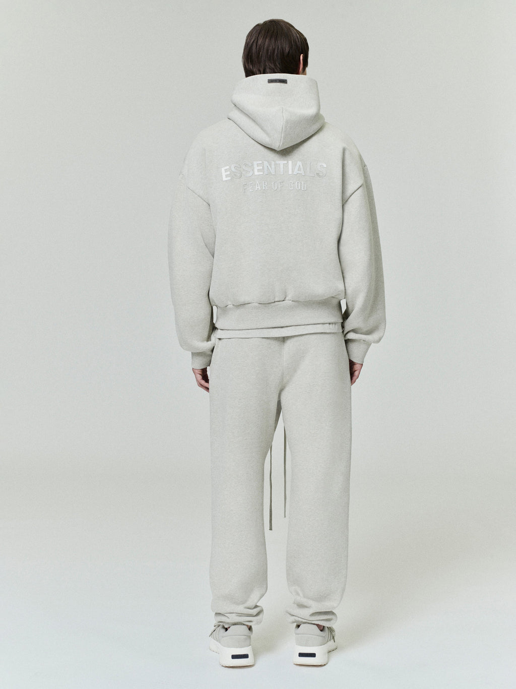rear view of light grey classic fleece hoodie with ESSENTIALS Fear of God logo and matching sweatpants on model